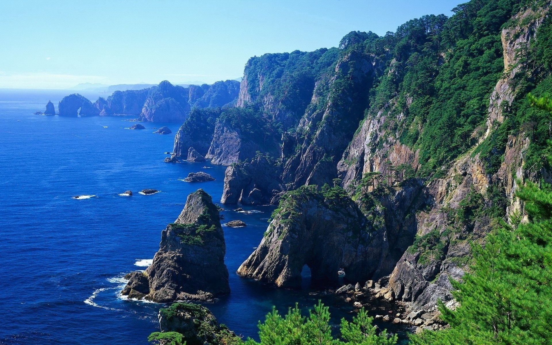 Jagged cliffs and blue ocean with rock formations HD Wallpaper