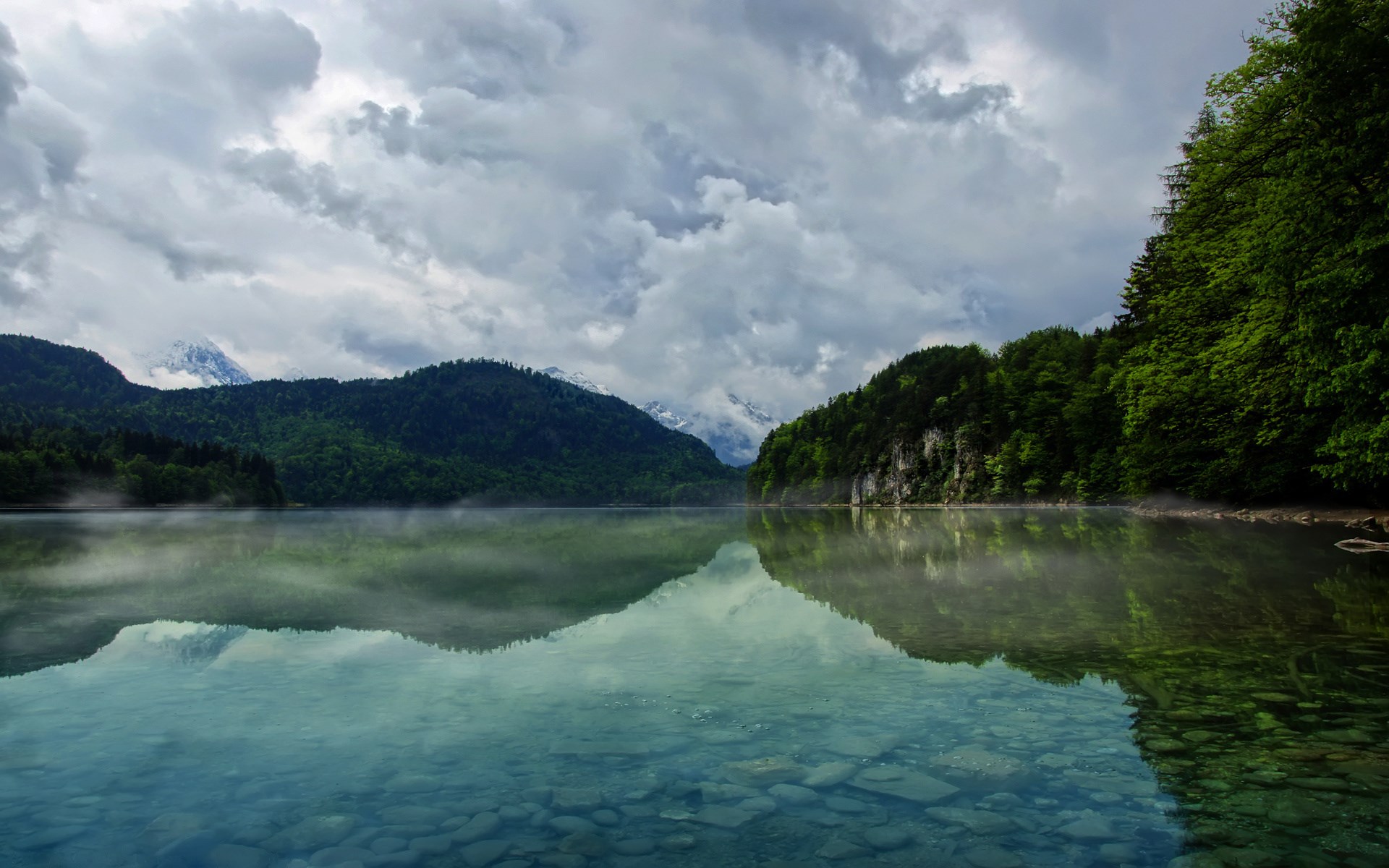 Misty lake reflecting mountains and forest under cloudy sky HD Wallpaper