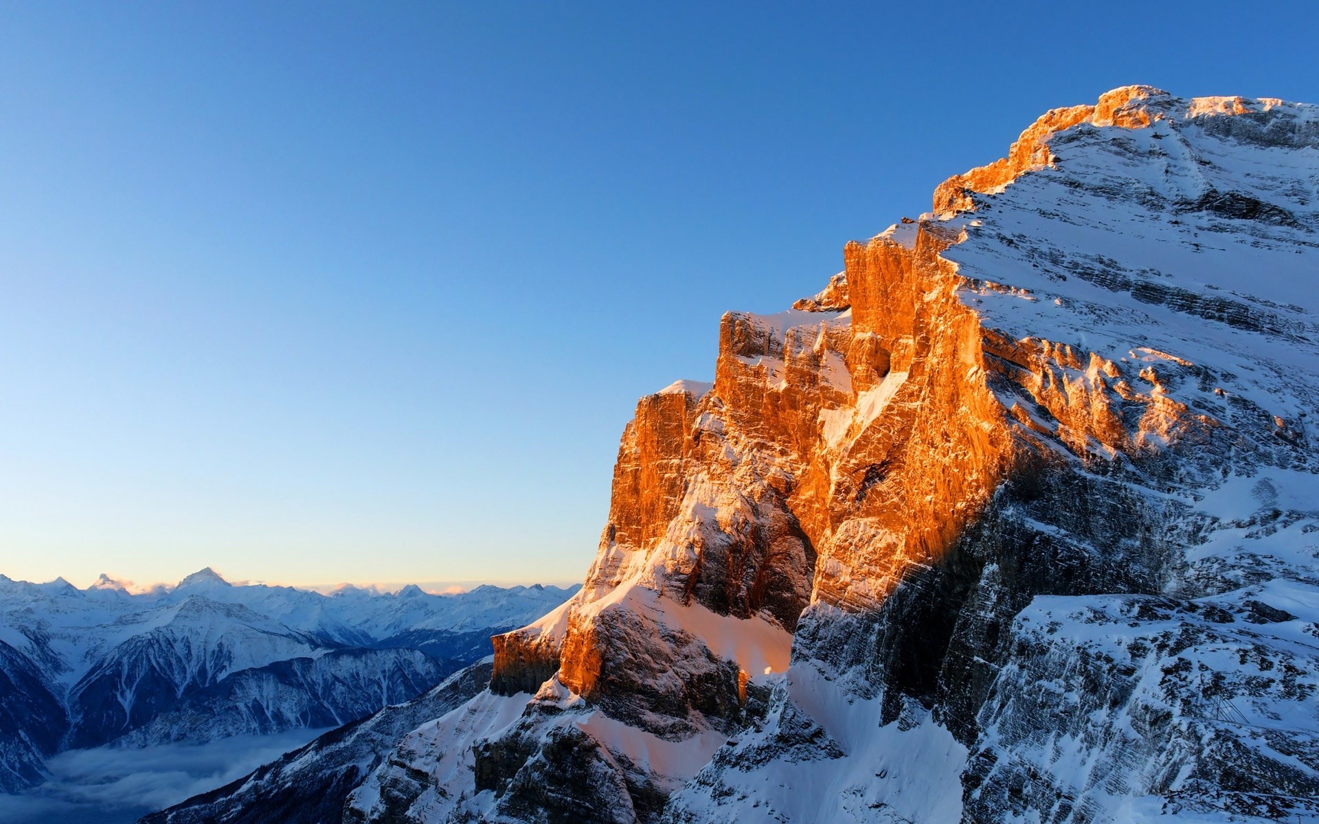 Snow-covered mountain peak illuminated by golden sunlight HD Wallpaper