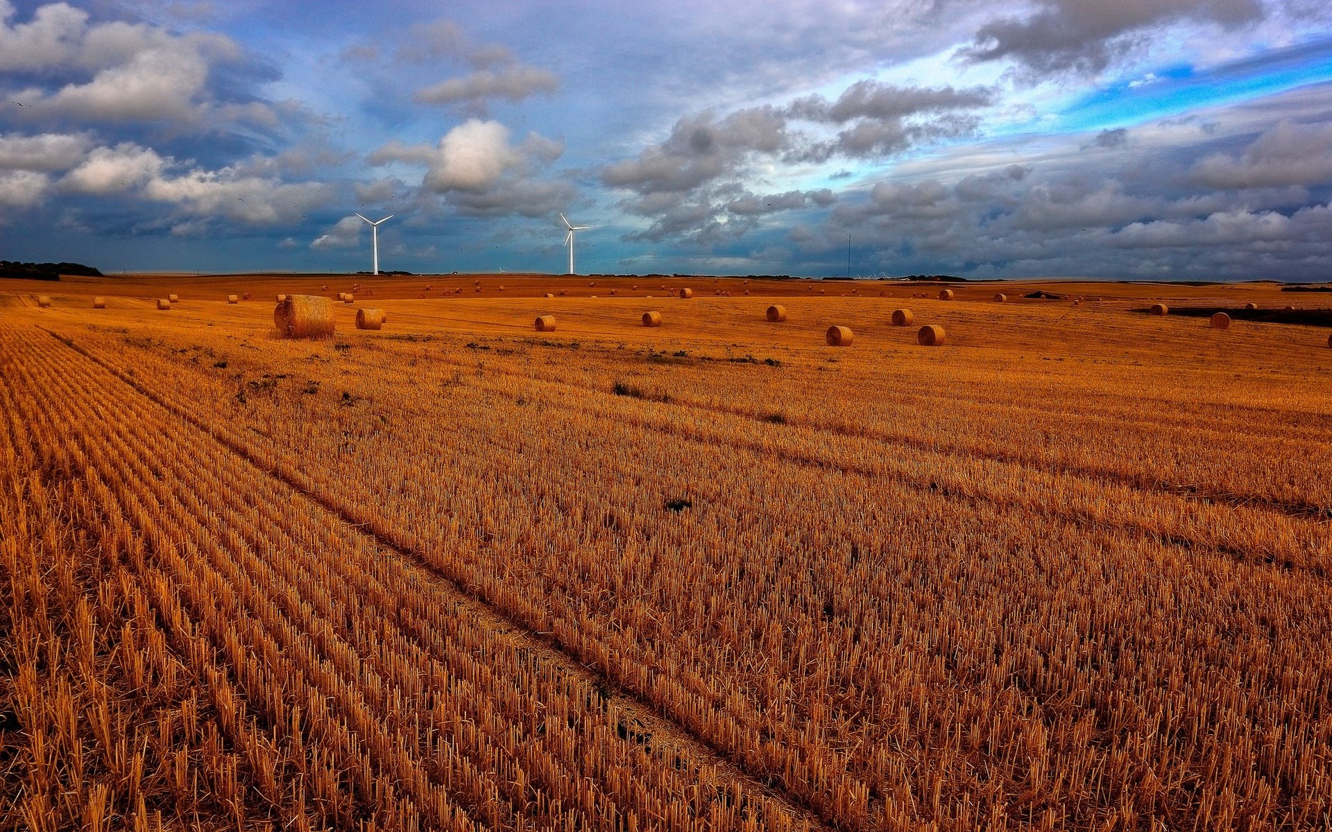 Wind turbines in a harvested wheat field with hay bales HD Wallpaper