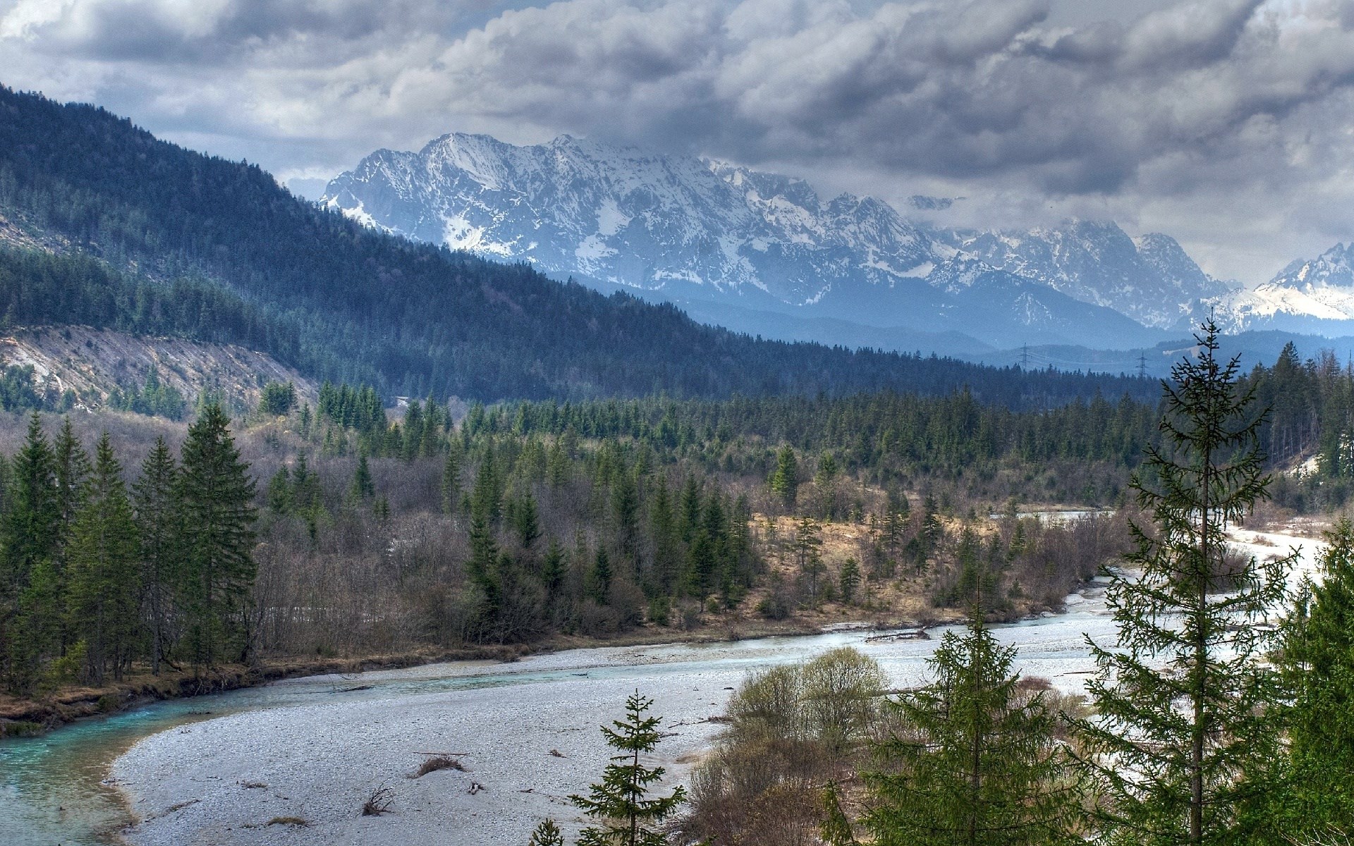 River flowing through a forest with snow-capped mountains in the background HD Wallpaper