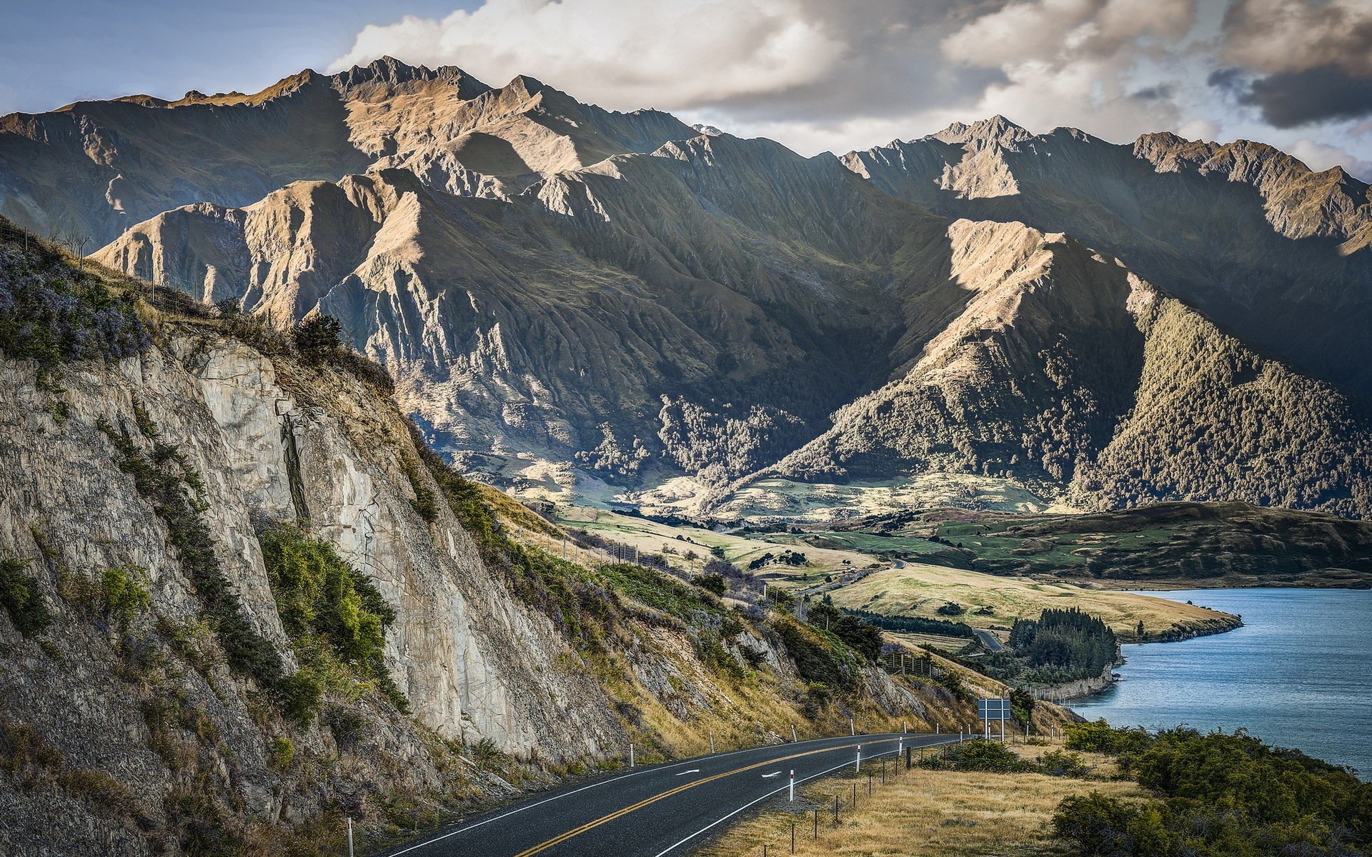 Mountain road next to a lake and mountains HD Wallpaper