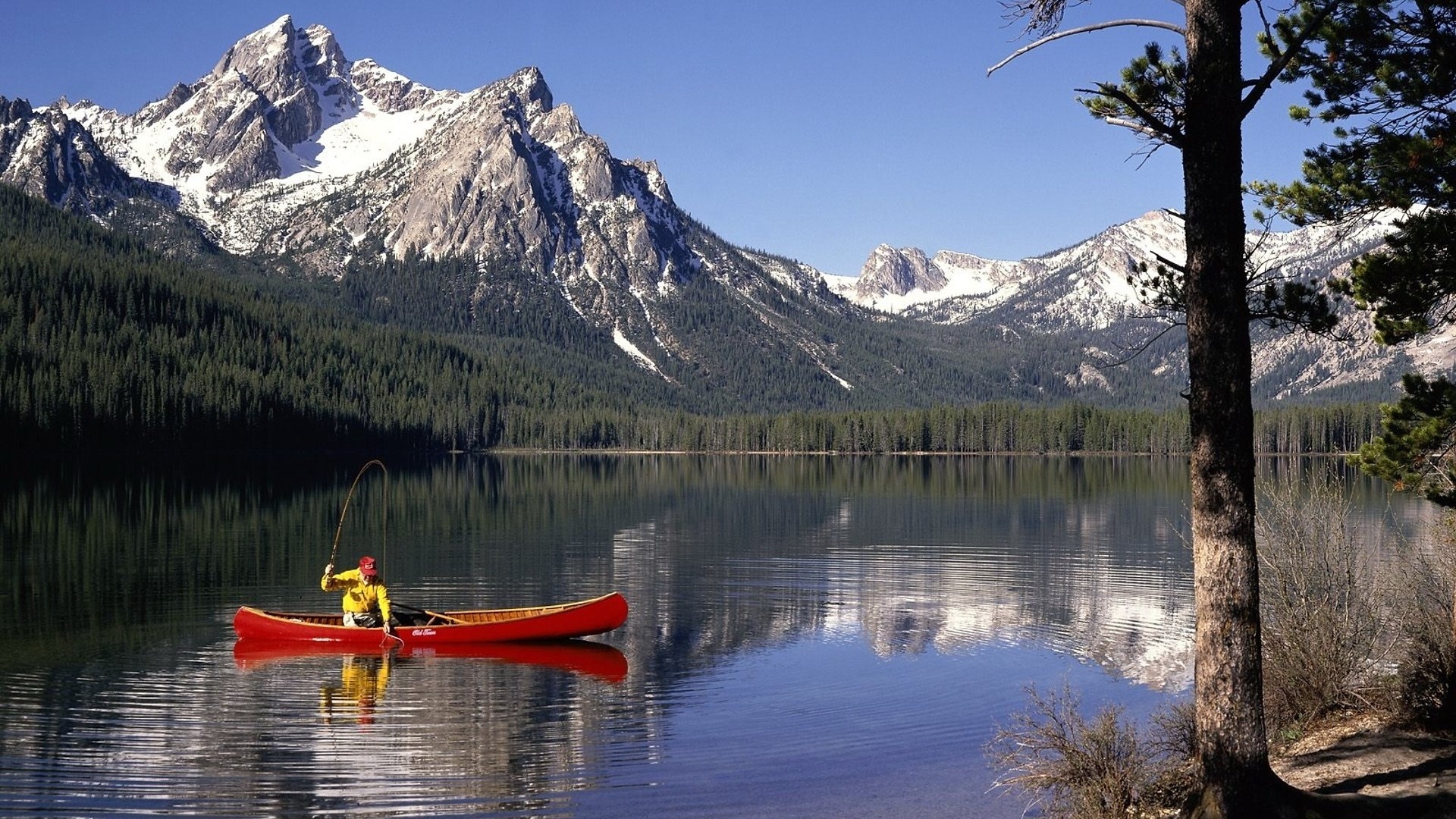 Man fishing from canoe on a lake with mountains HD Wallpaper