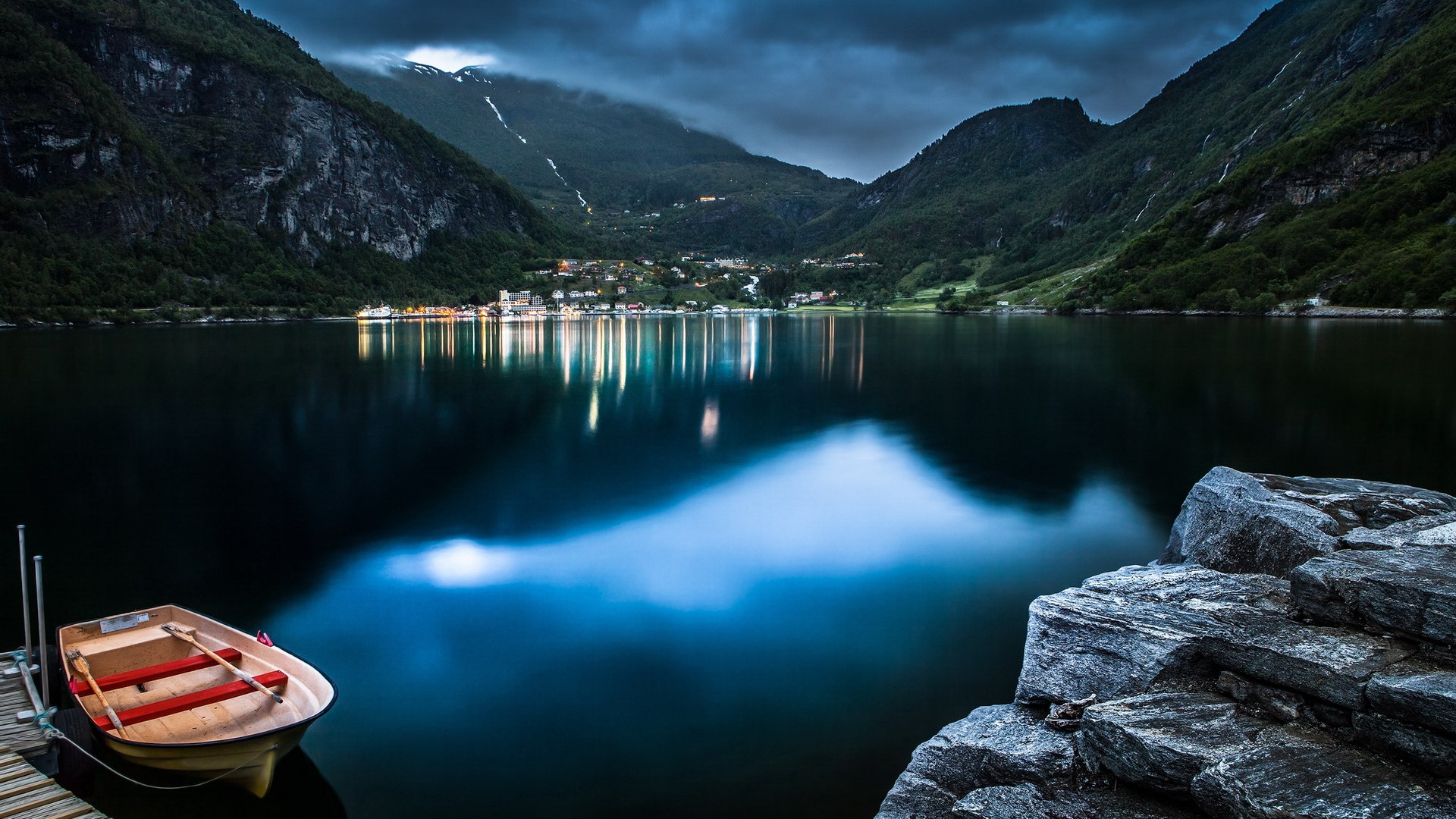 Boat docked on a lake with a village in the background HD Wallpaper