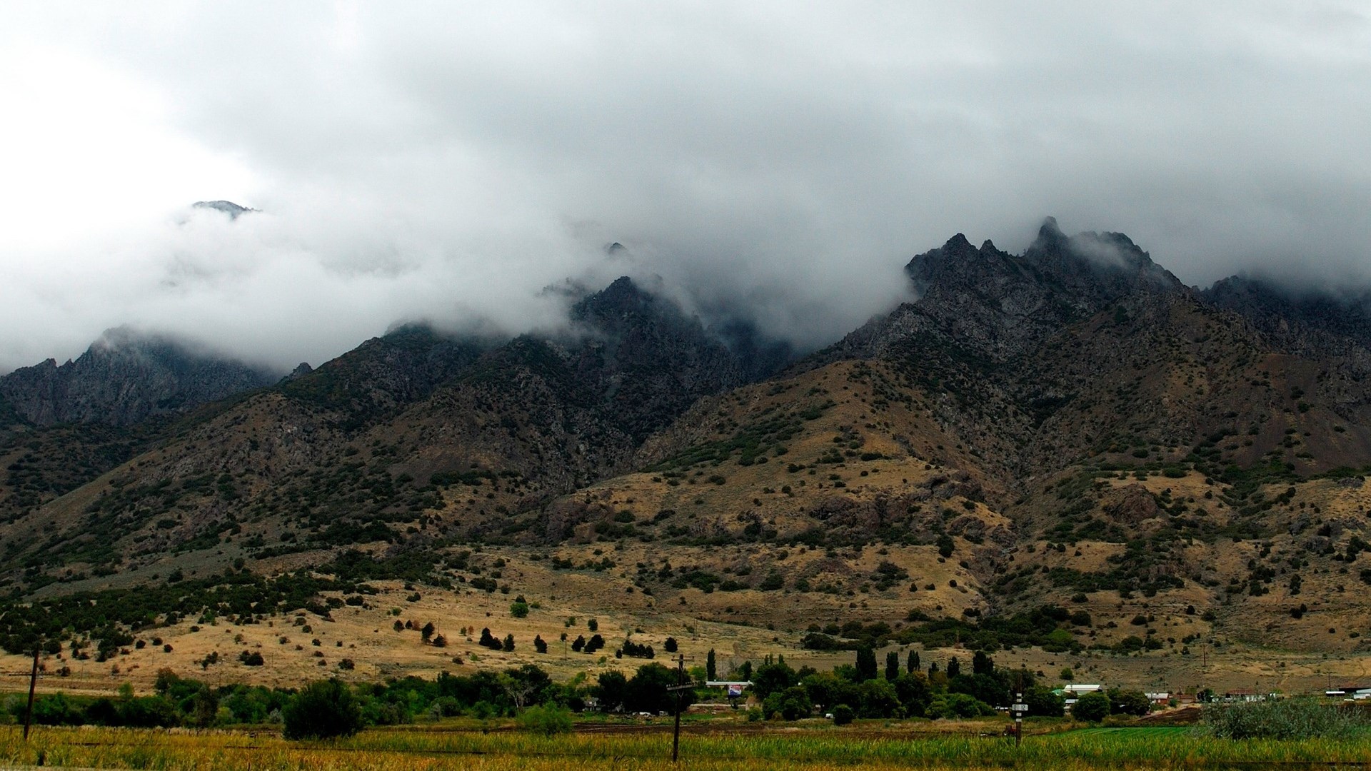 Misty mountains with scattered trees and buildings HD Wallpaper