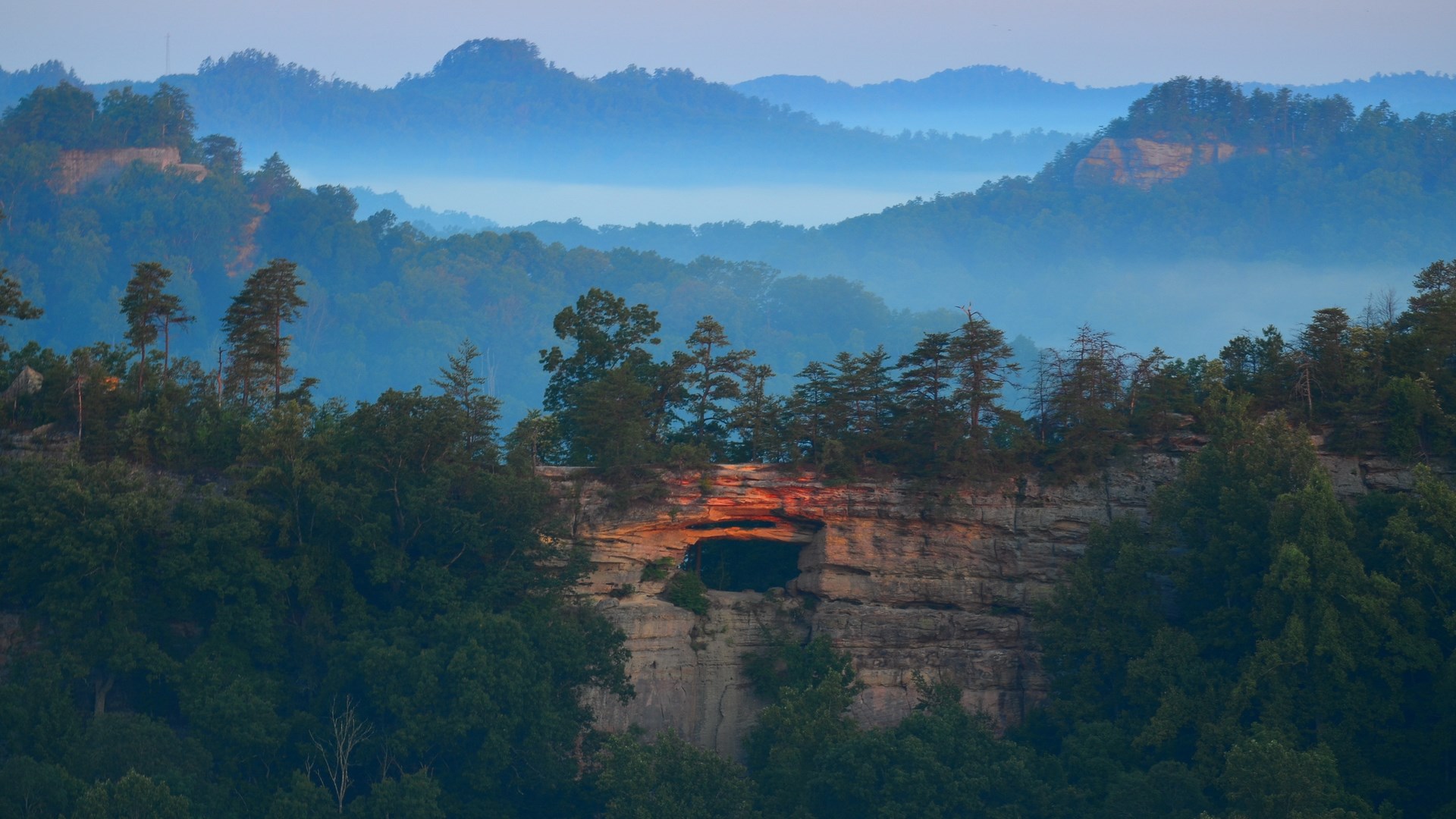 Natural rock arch with trees and misty mountains HD Wallpaper