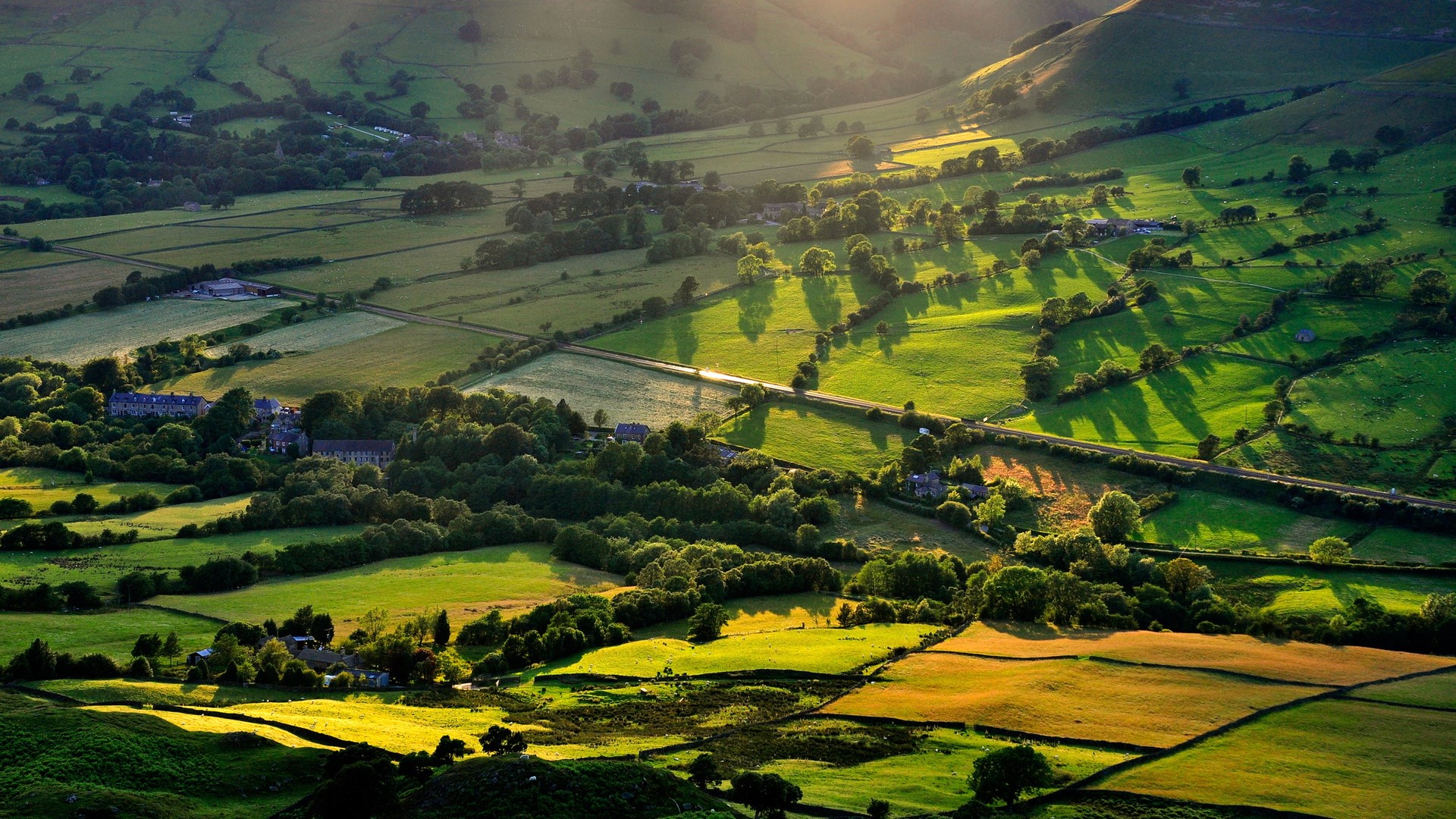 Rolling green hills with scattered trees and buildings HD Wallpaper