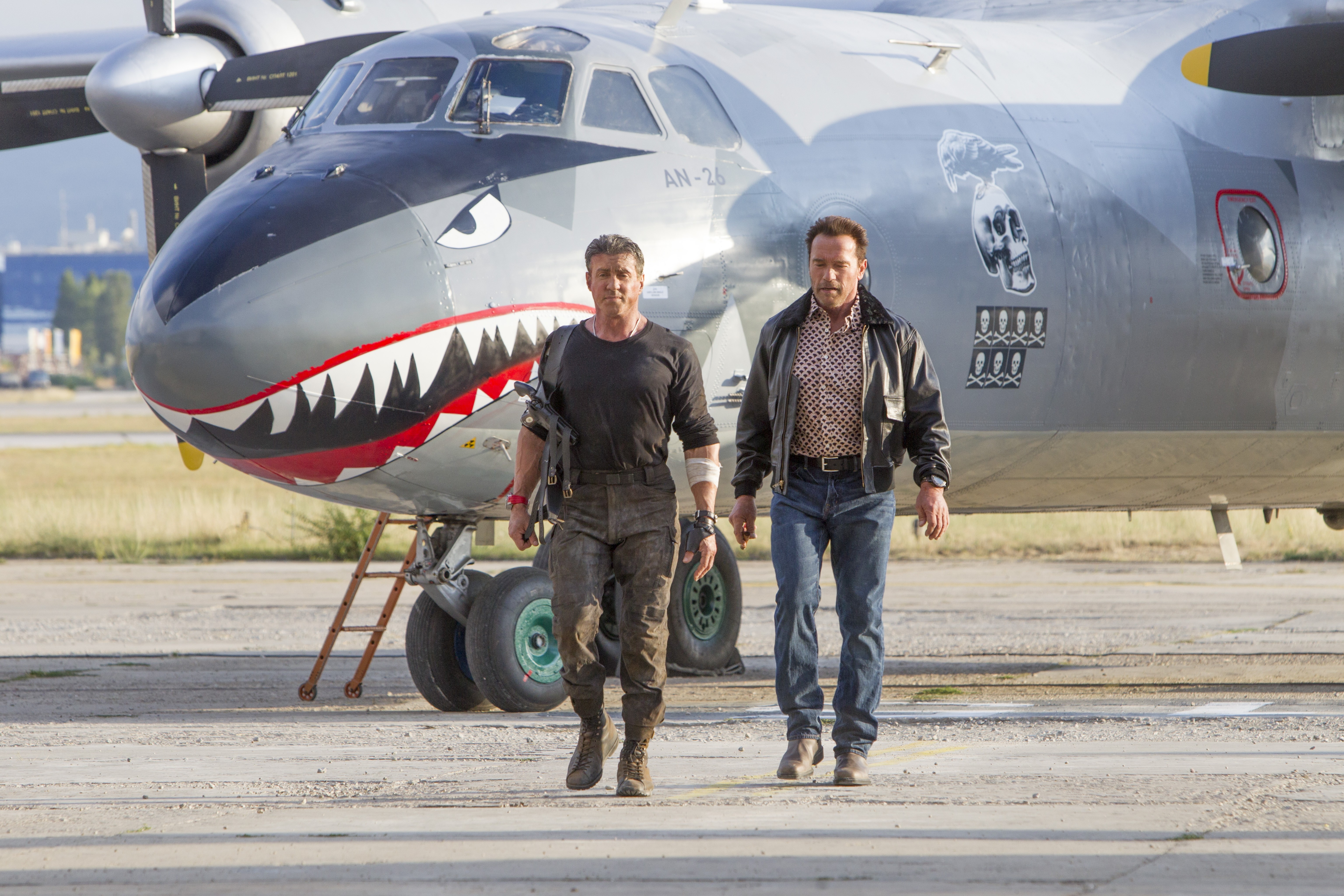 Sylvester Stallone and Arnold Schwarzenegger walk past an AN-26 airplane HD Wallpaper