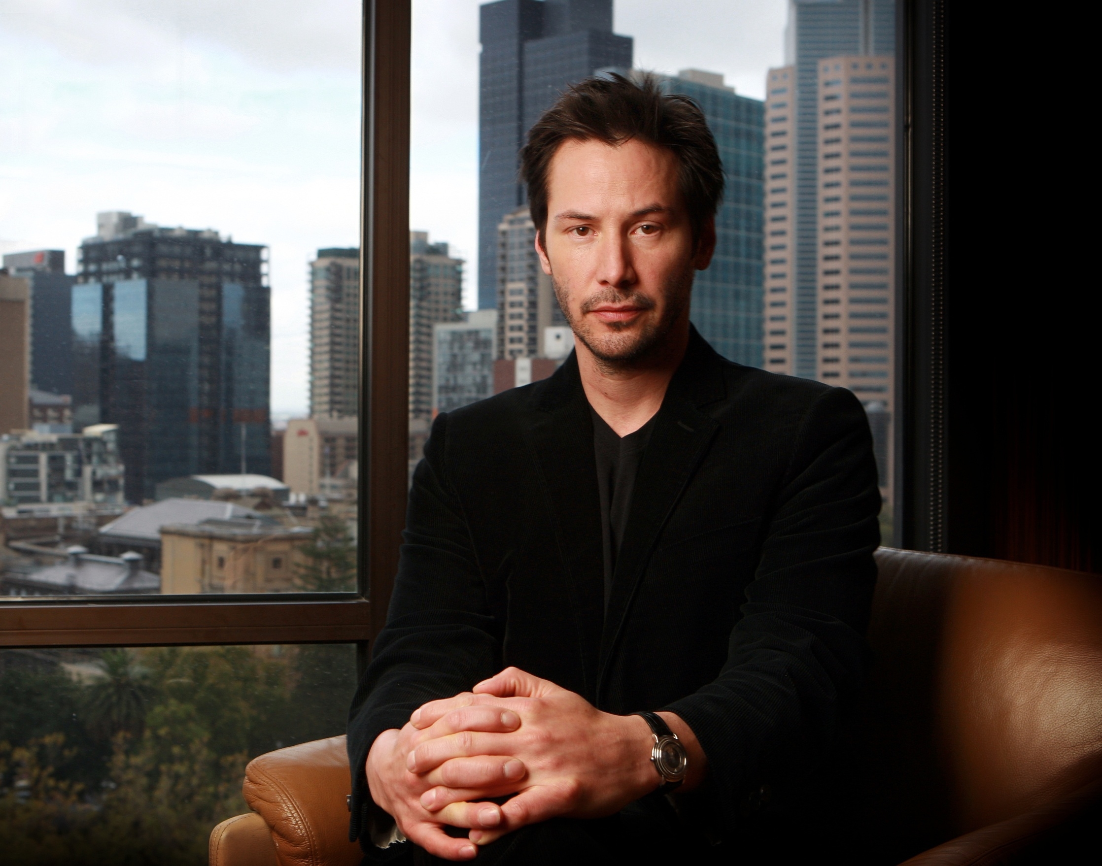 Keanu Reeves sitting in front of a city skyline HD Wallpaper