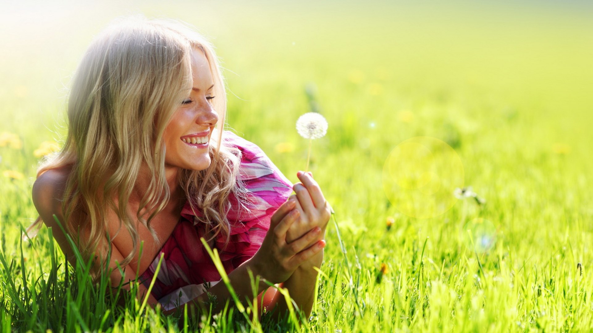 Woman lying in grass holding a dandelion HD Wallpaper