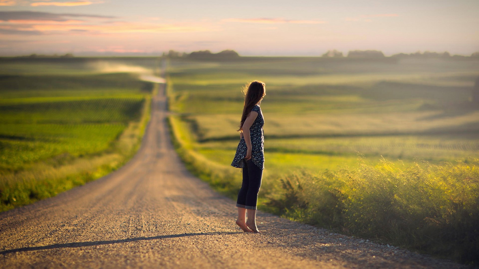 Girl standing on a dirt road in a field at sunset HD Wallpaper