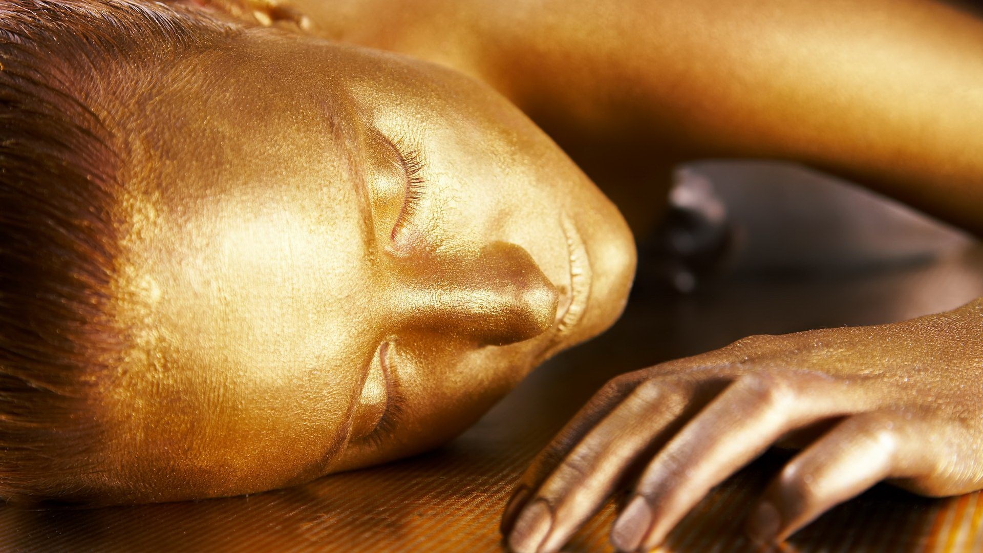Woman covered in gold paint lying down HD Wallpaper