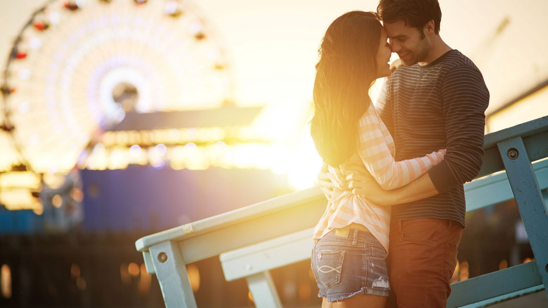 Couple embracing on a pier with a Ferris wheel HD Wallpaper