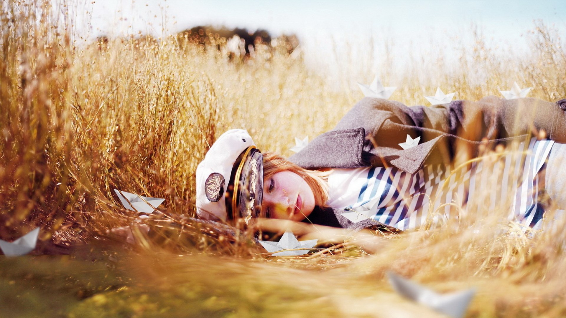 Girl in sailor hat lying in tall grass with paper boats HD Wallpaper