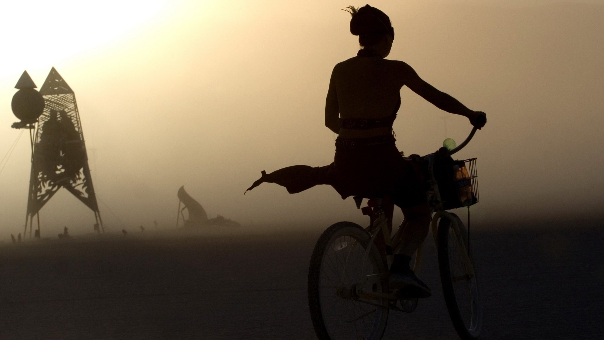 Woman on bicycle in dusty desert landscape HD Wallpaper