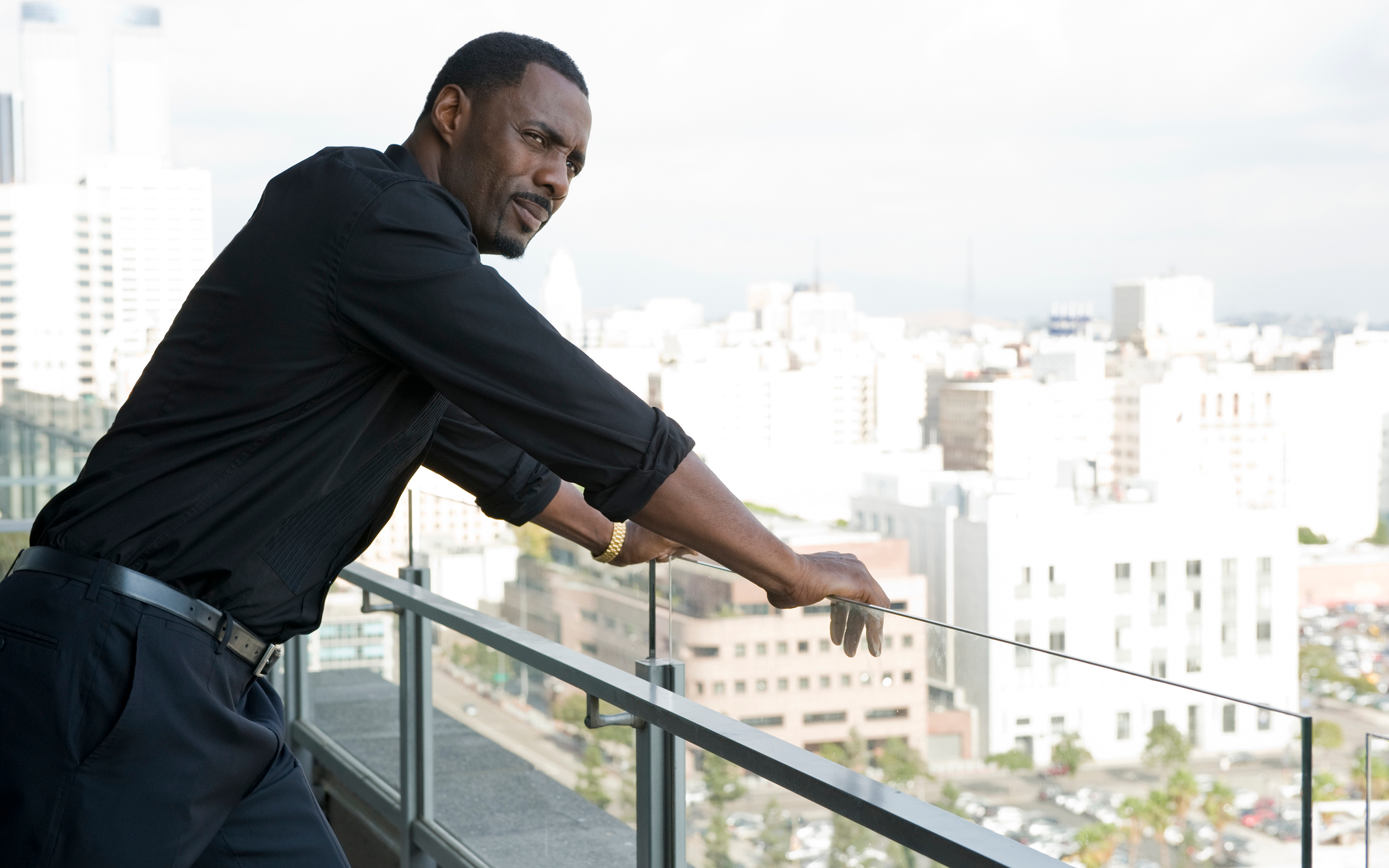 Idris Elba on a balcony overlooking a city HD Wallpaper
