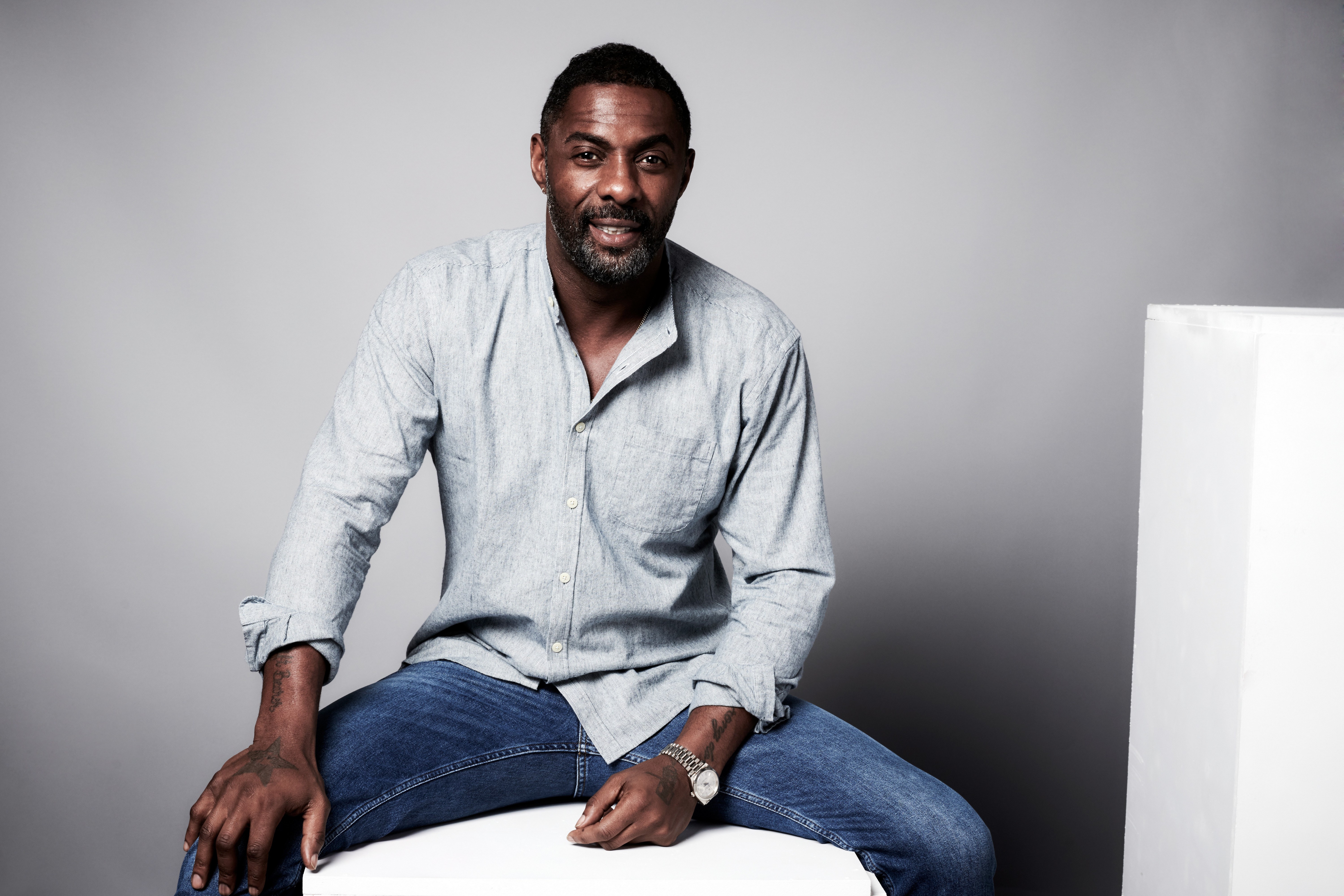 Idris Elba sitting on a white cube HD Wallpaper