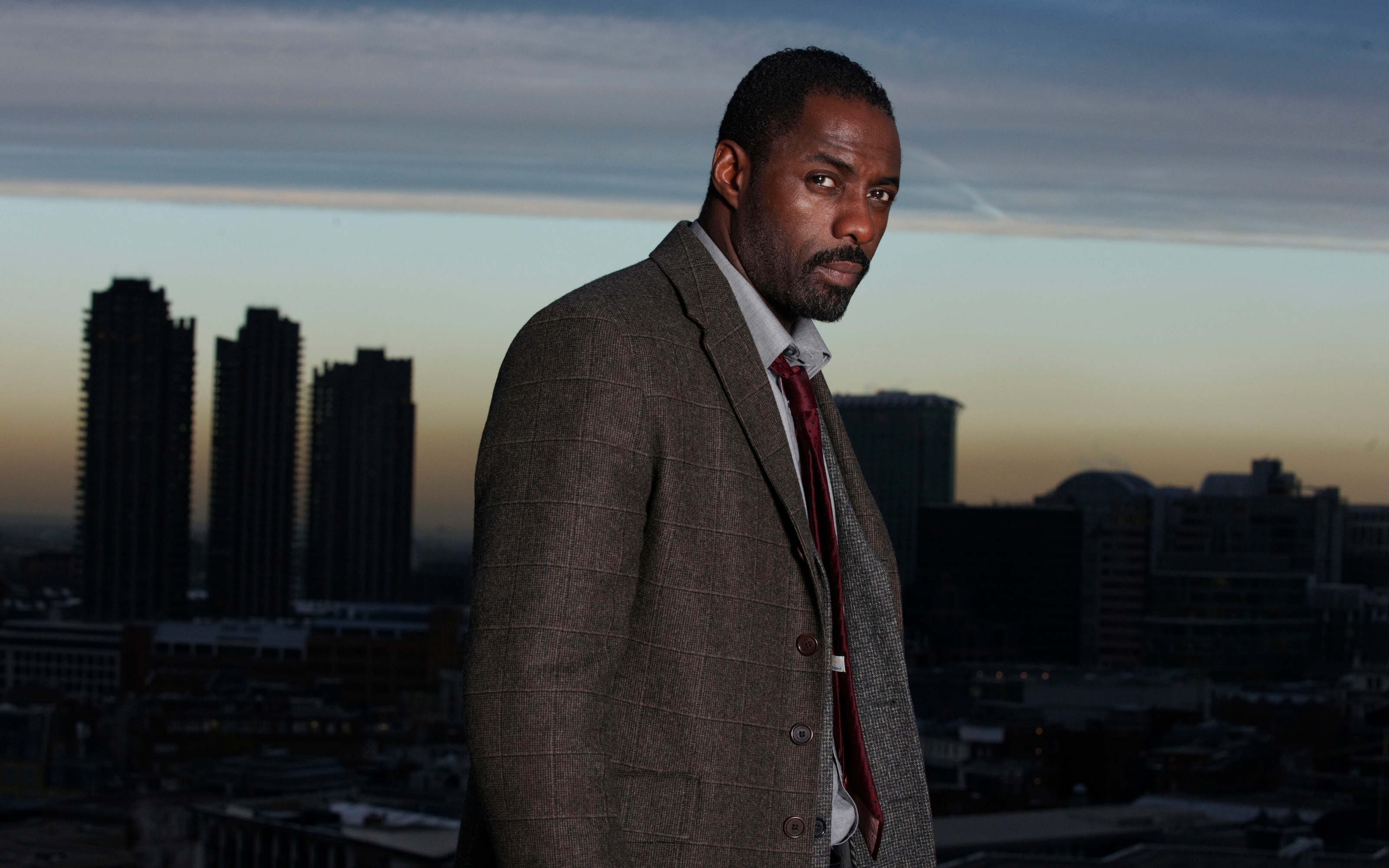 Idris Elba in a suit with city skyline HD Wallpaper