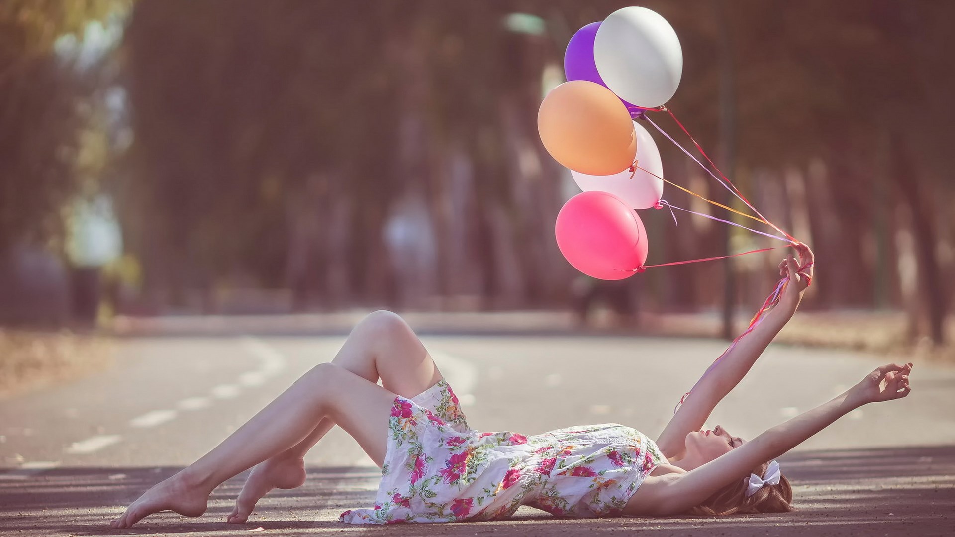 Woman lying on road holding balloons HD Wallpaper
