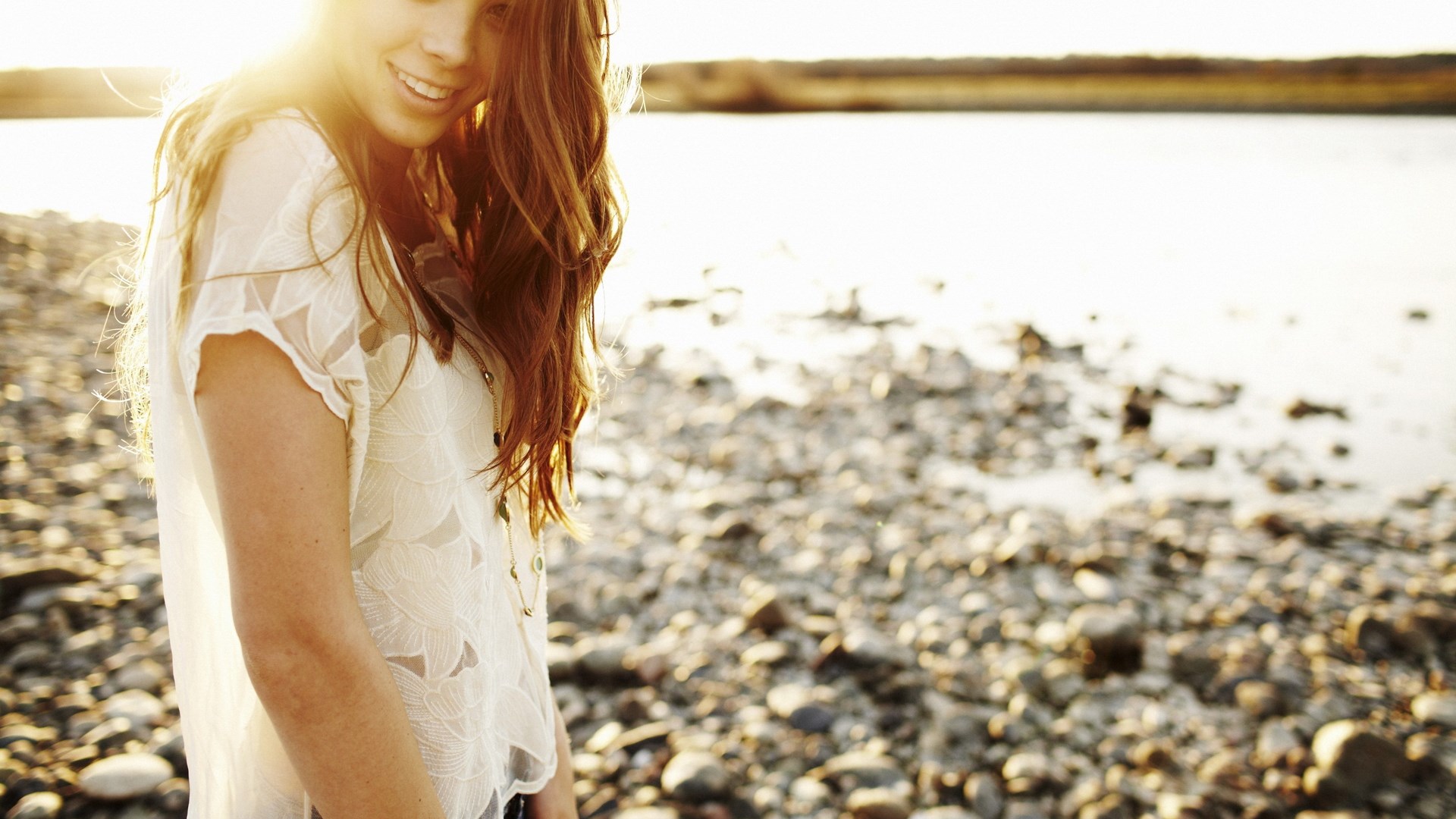 Woman smiling on a rocky beach at sunset HD Wallpaper