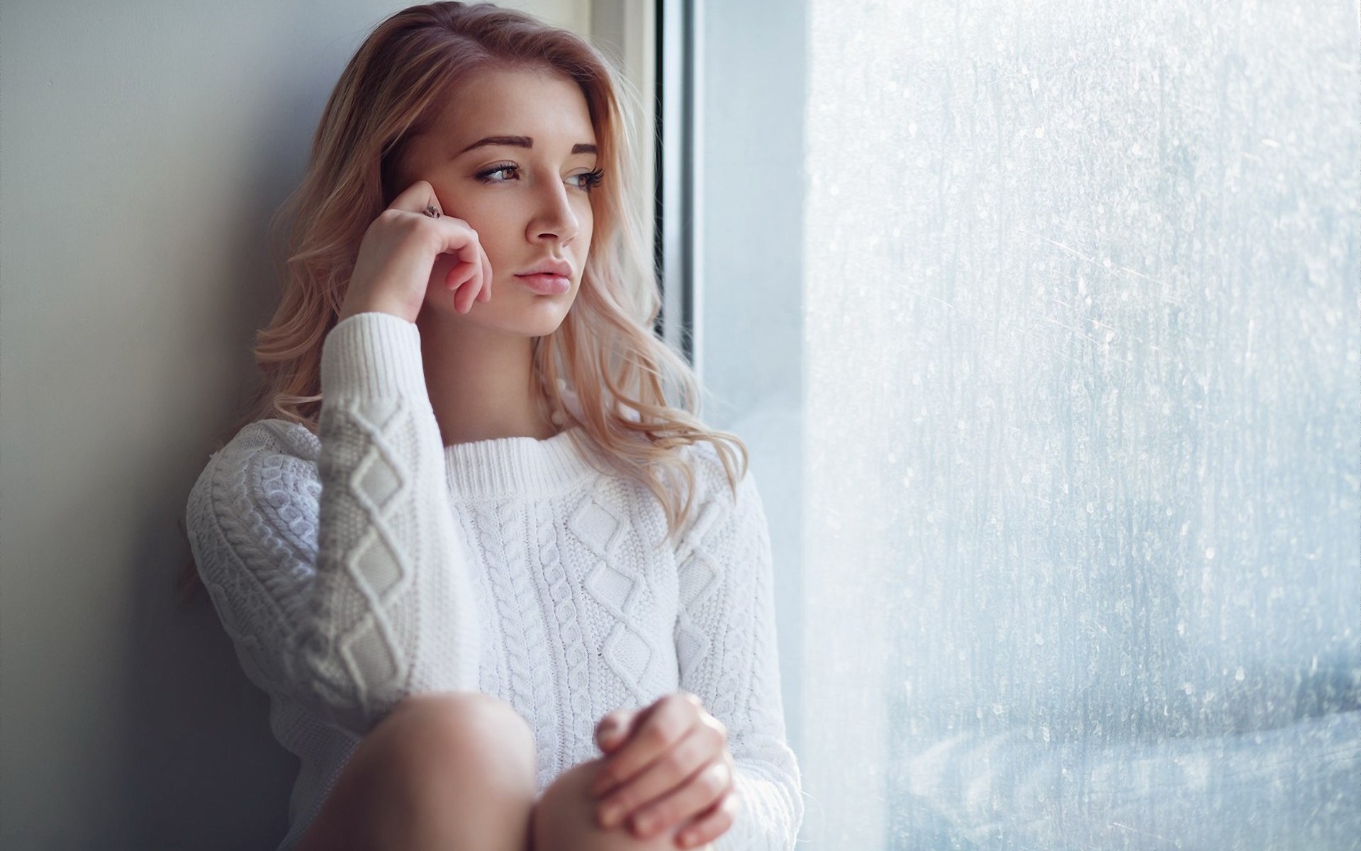 Woman in white sweater looking out a window HD Wallpaper