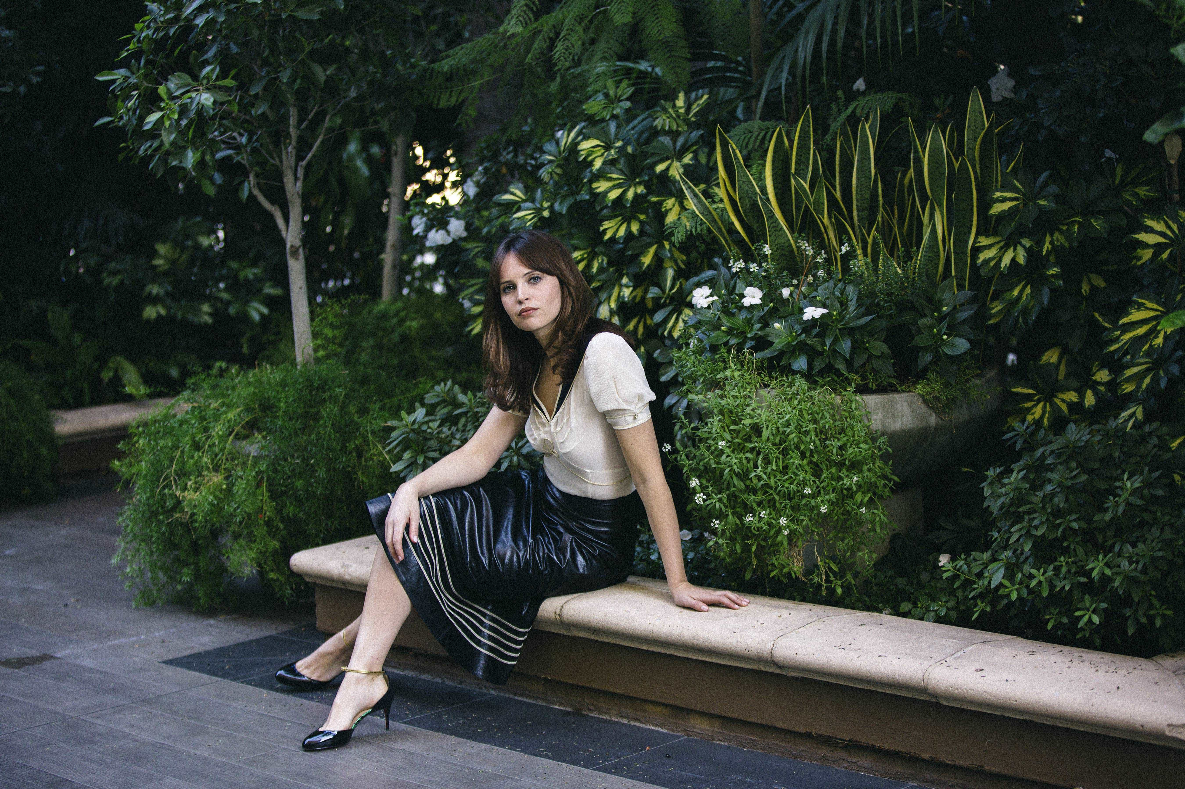 Felicity Jones sitting on a bench in a garden HD Wallpaper