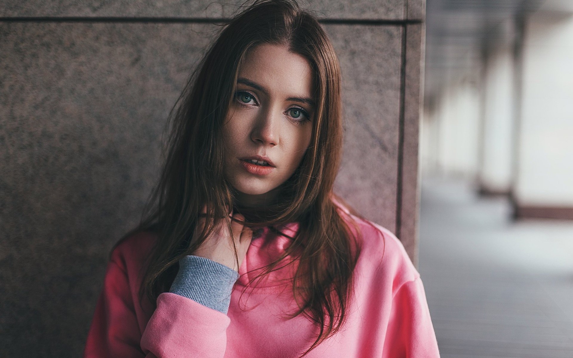 Young woman in pink hoodie touching her neck HD Wallpaper