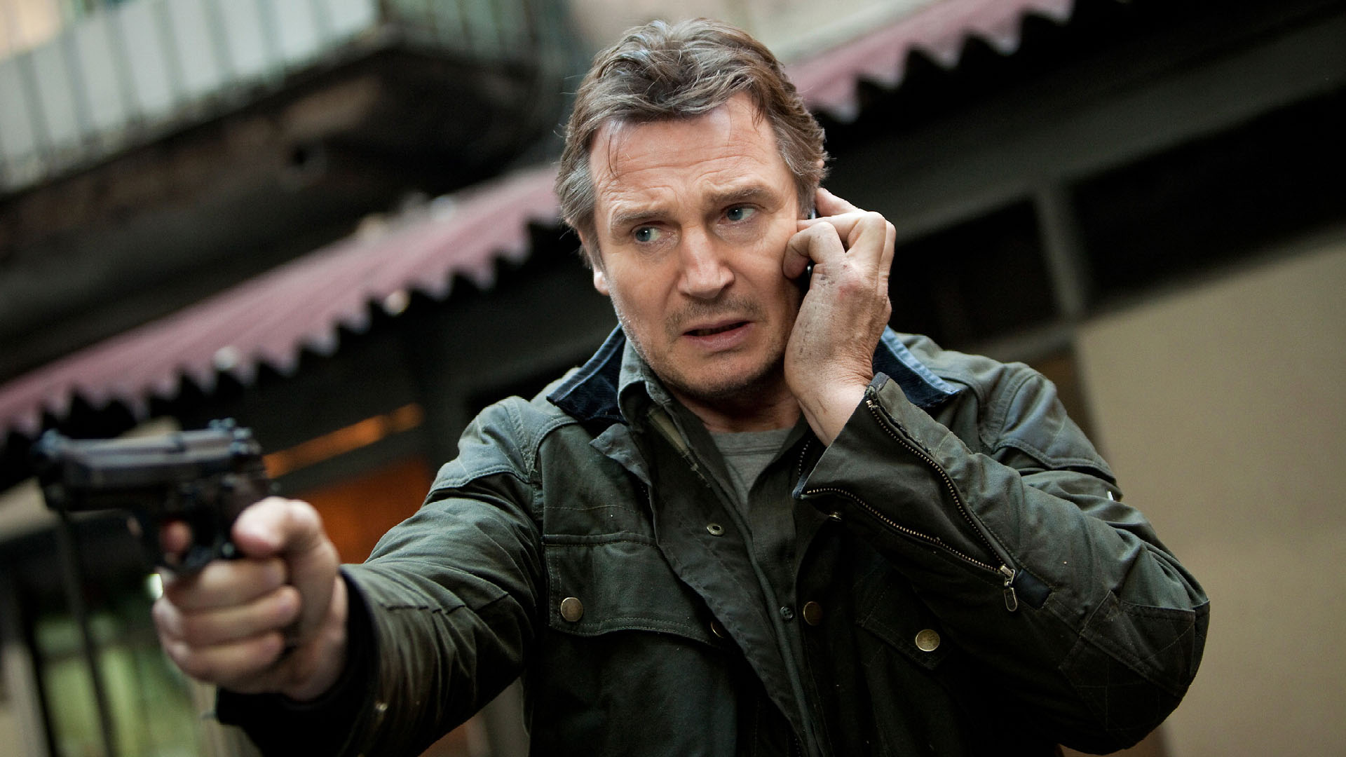 Liam Neeson holding a gun and talking on the phone HD Wallpaper