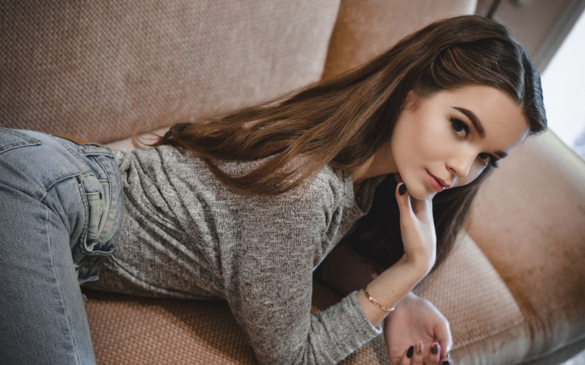 Woman in grey sweater and jeans lying on couch HD Wallpaper