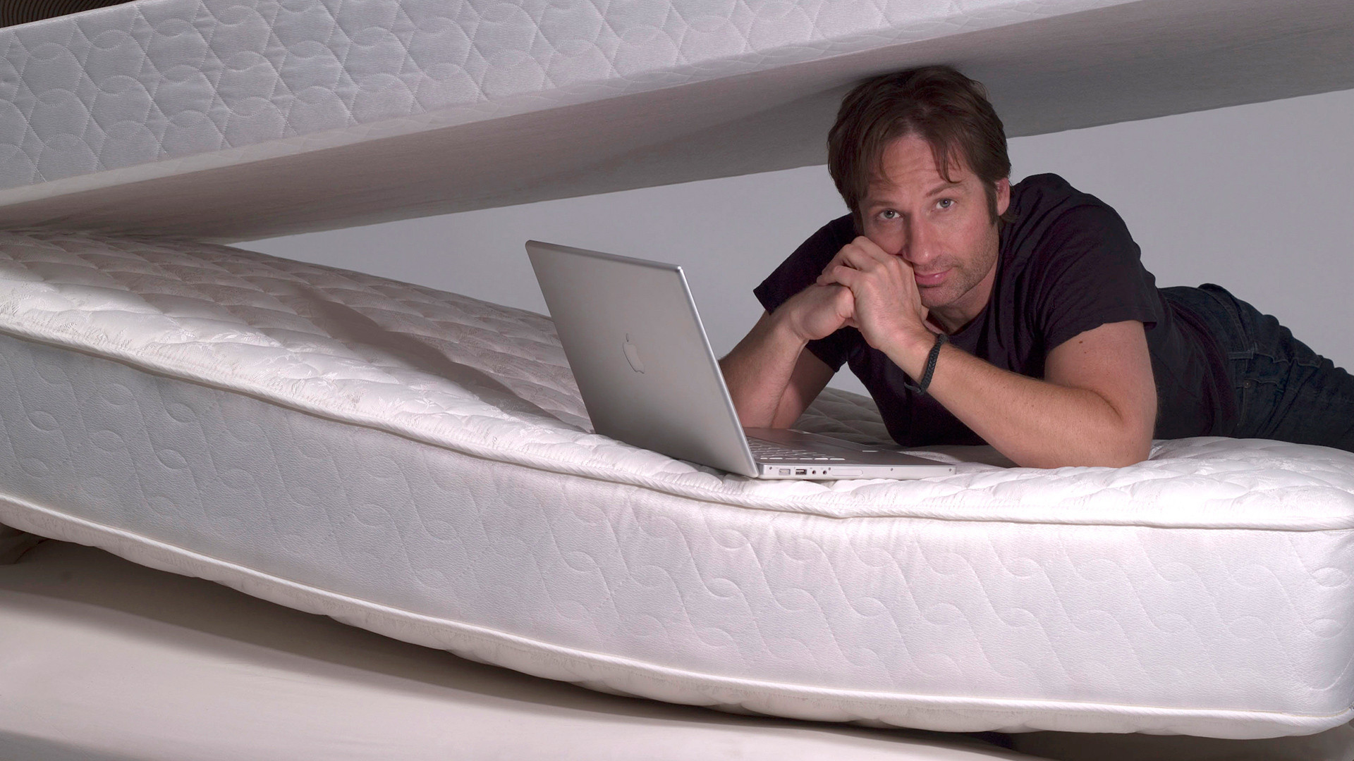 David Duchovny lying on mattresses with laptop HD Wallpaper