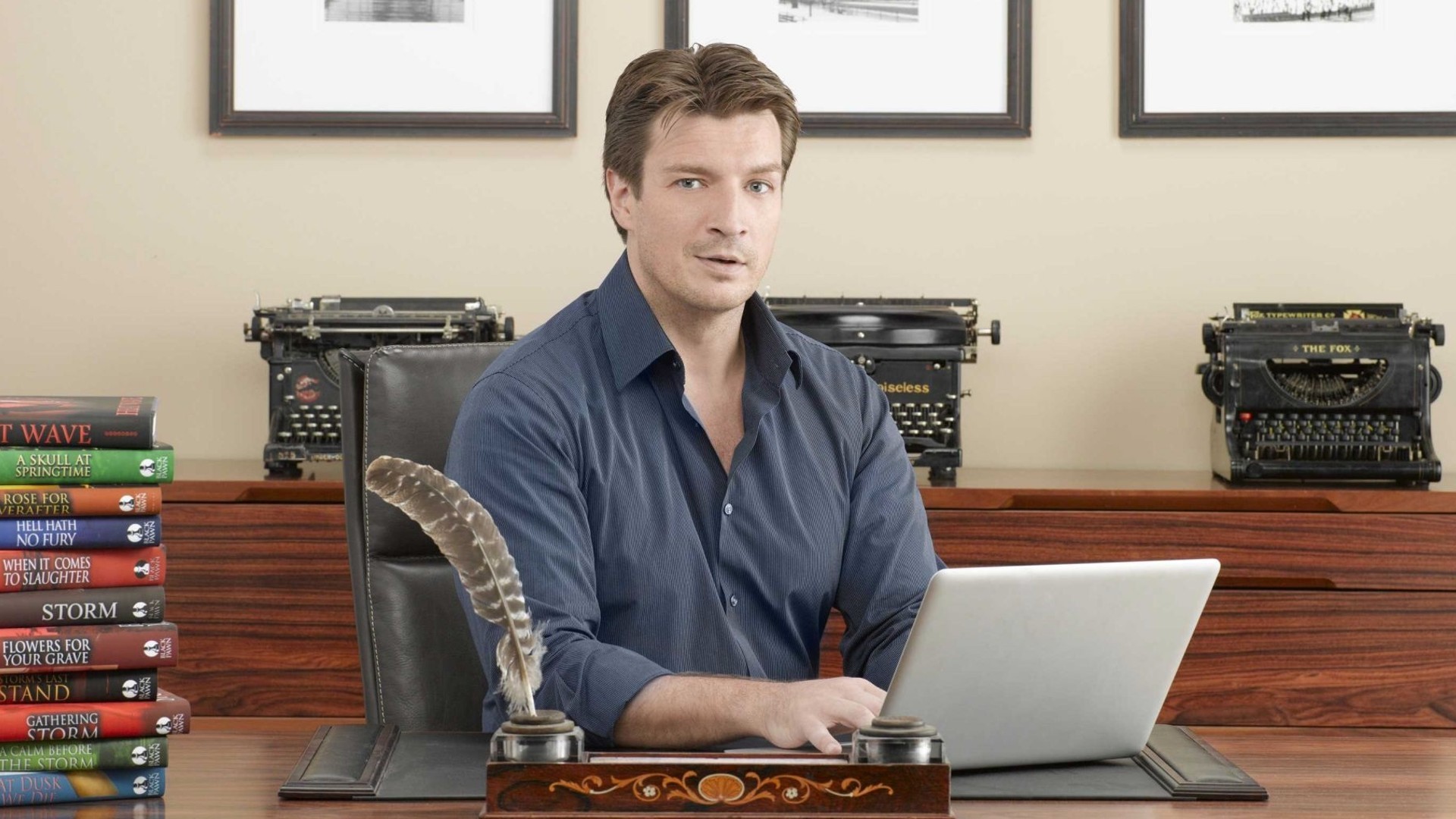 Nathan Fillion at a desk with typewriters and books HD Wallpaper