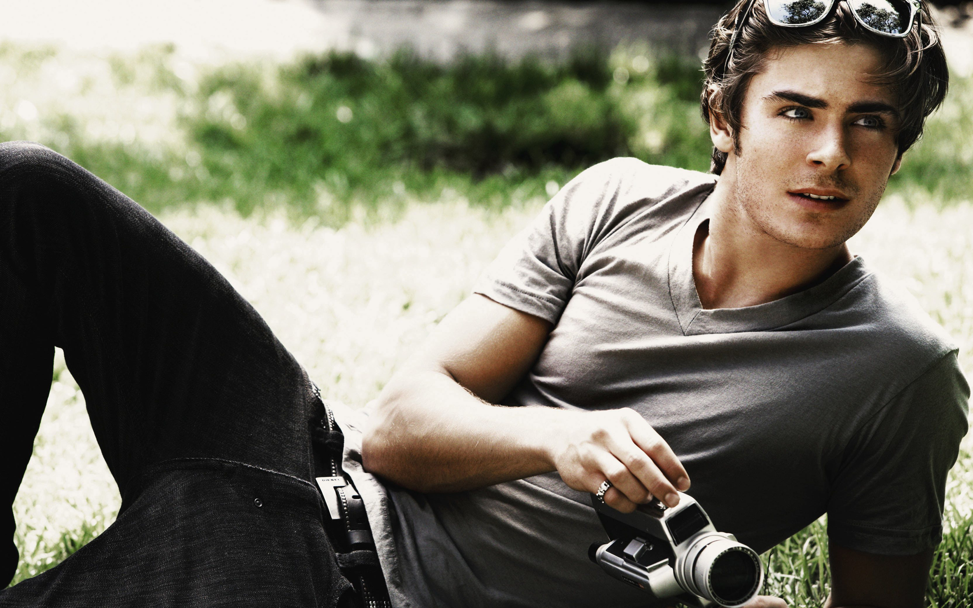 Zac Efron lying on grass with a camera HD Wallpaper