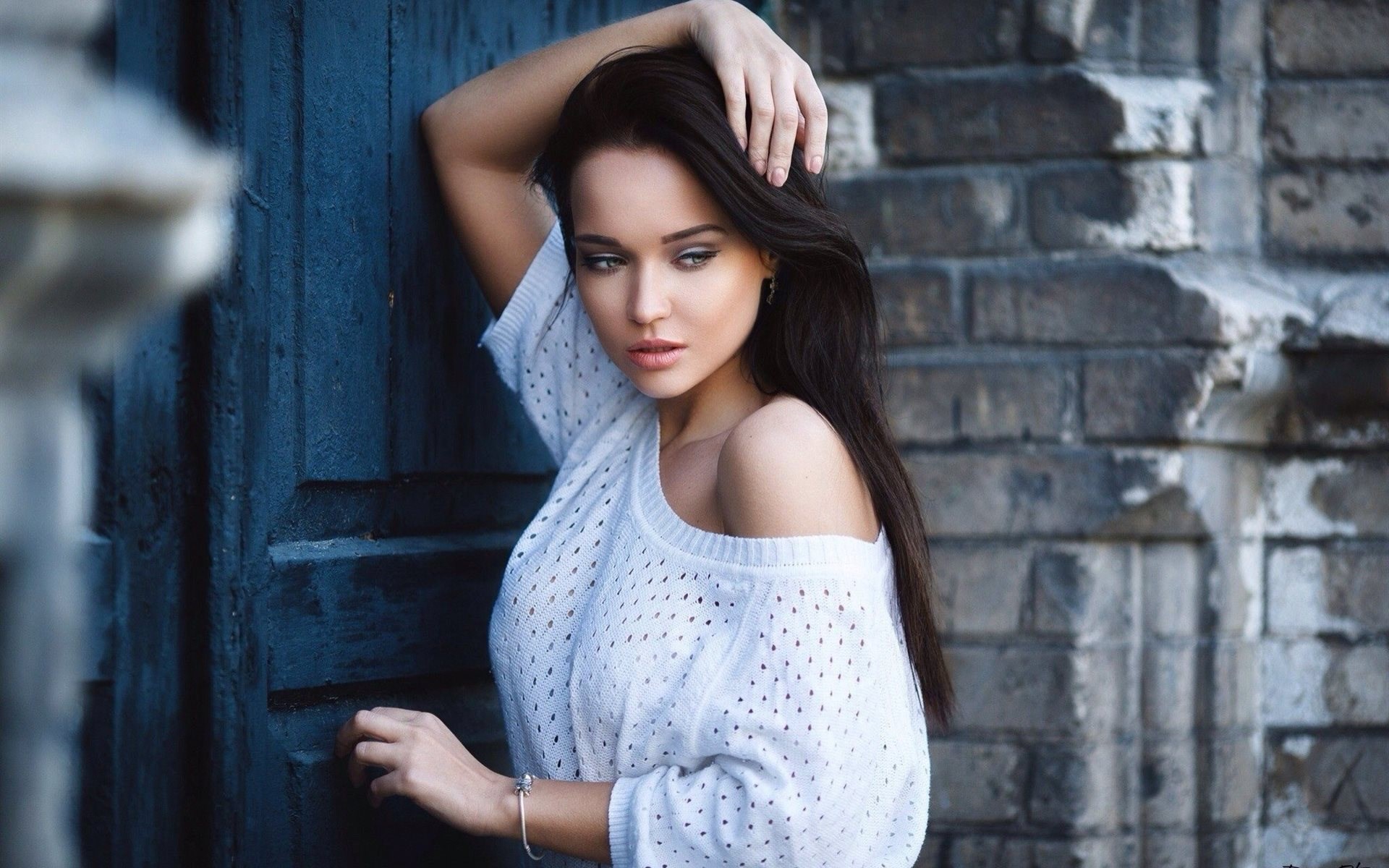 Woman in white sweater leaning against a blue wall HD Wallpaper