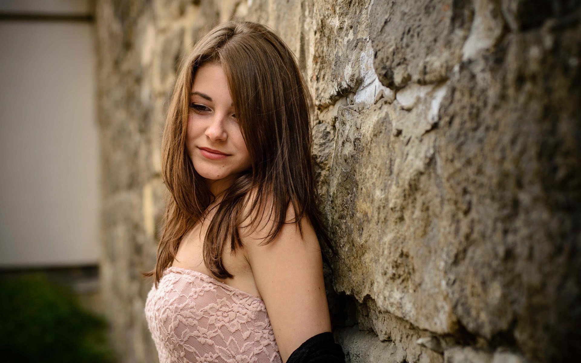 Young woman leaning against a stone wall HD Wallpaper