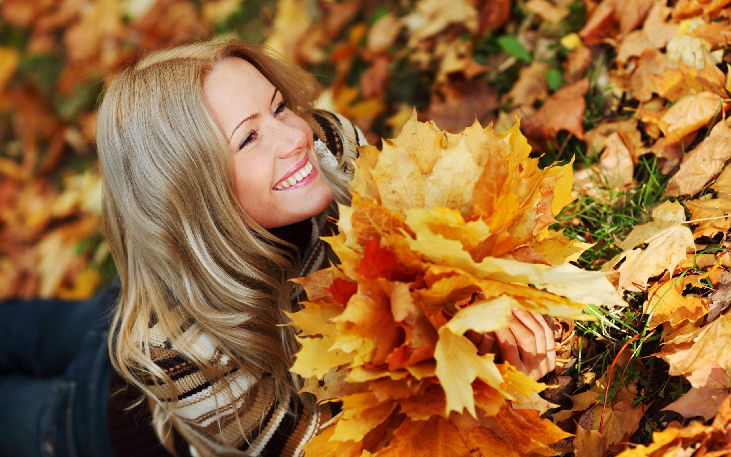 Woman lying in autumn leaves holding maple leaves HD Wallpaper