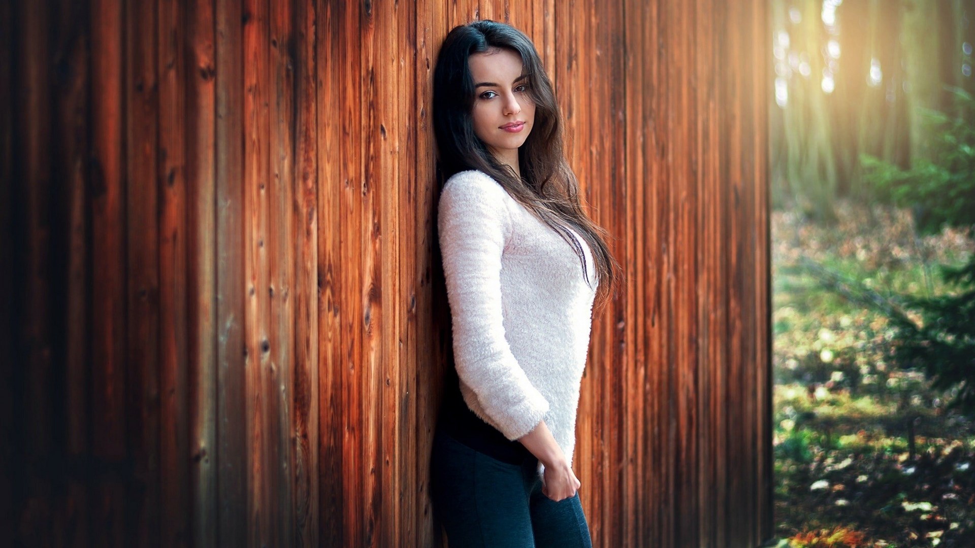 Woman leaning against a wooden wall in a forest HD Wallpaper