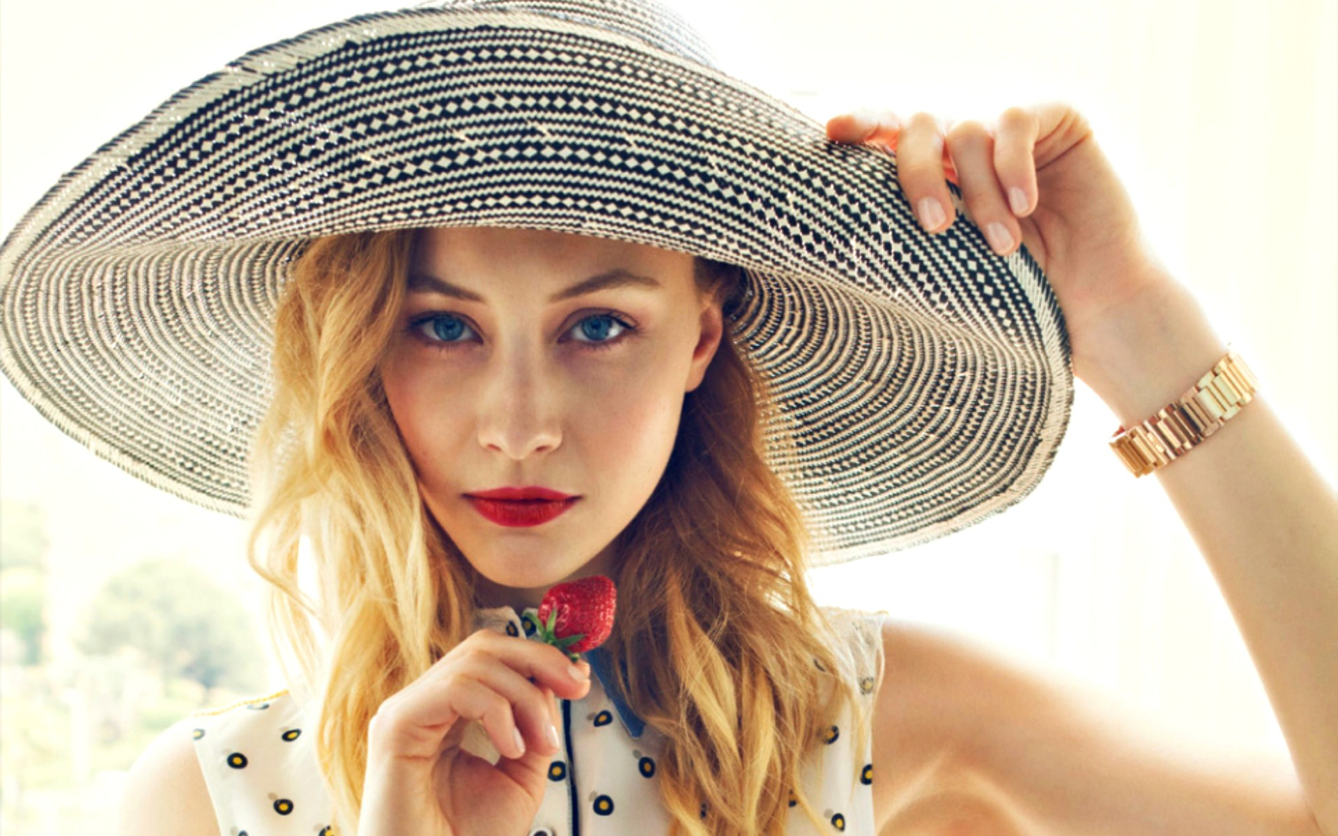 Sarah Gadon wearing a large hat and holding a strawberry HD Wallpaper