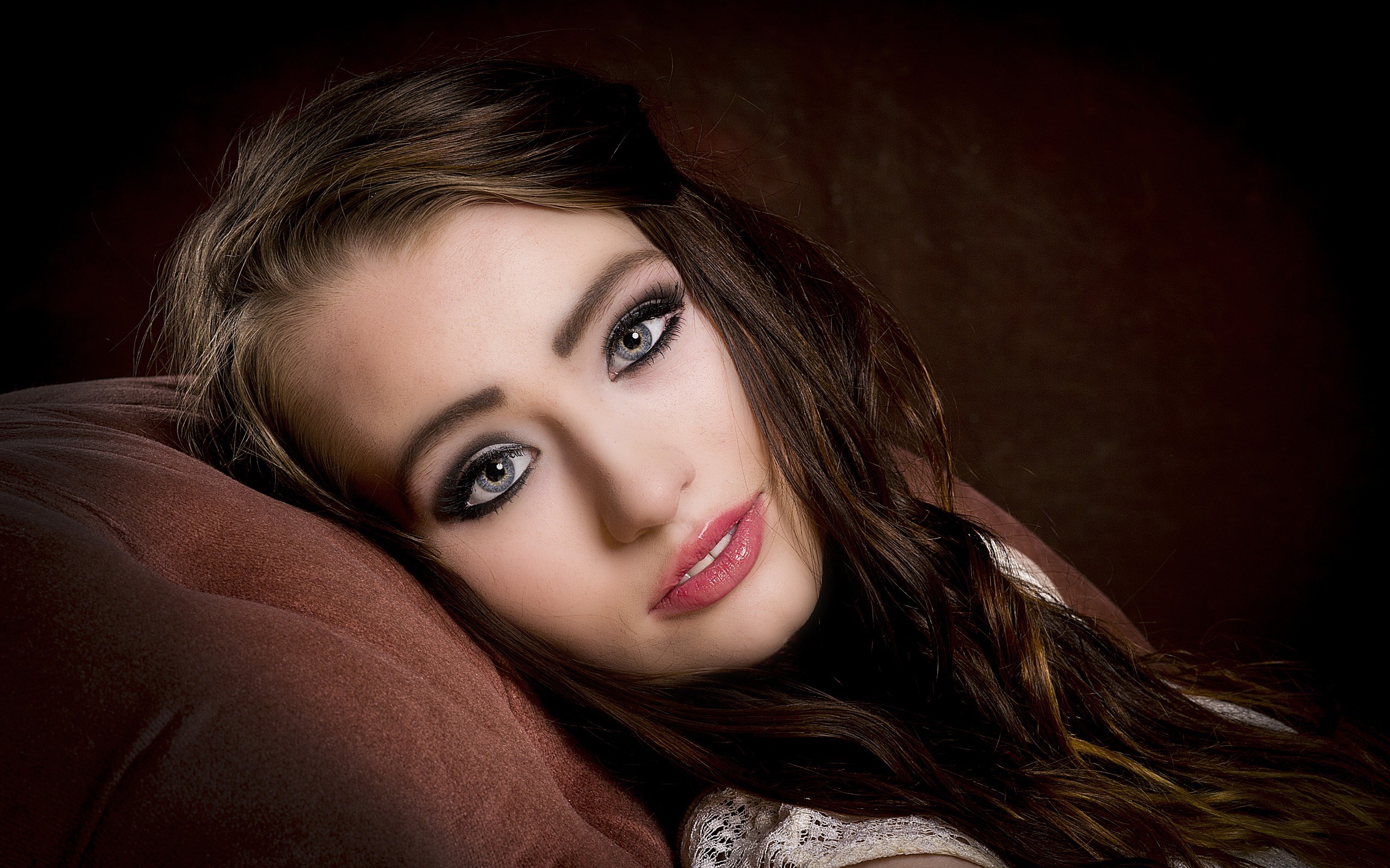 Woman with dark hair and makeup lying on a pillow HD Wallpaper