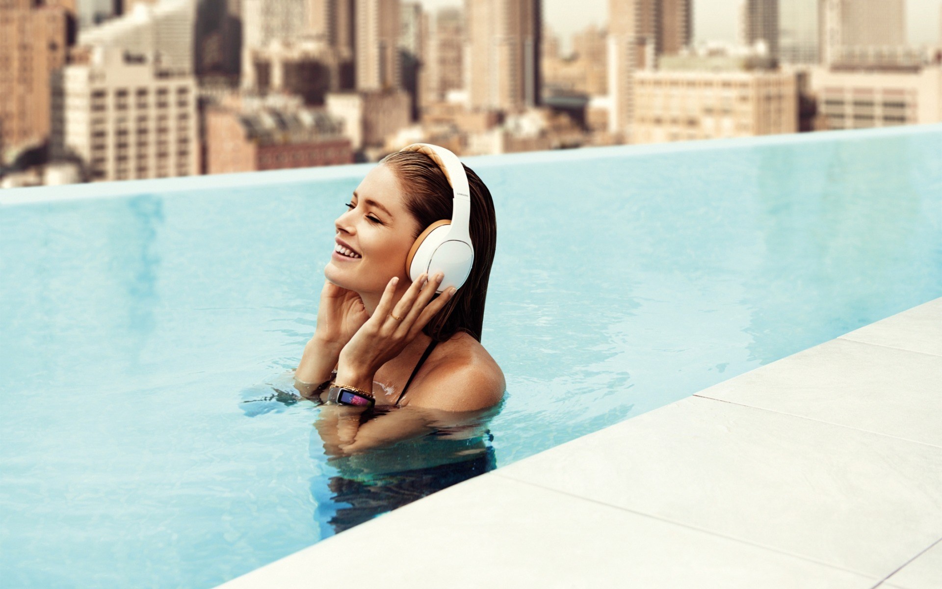 Woman in headphones in a pool with city skyline HD Wallpaper