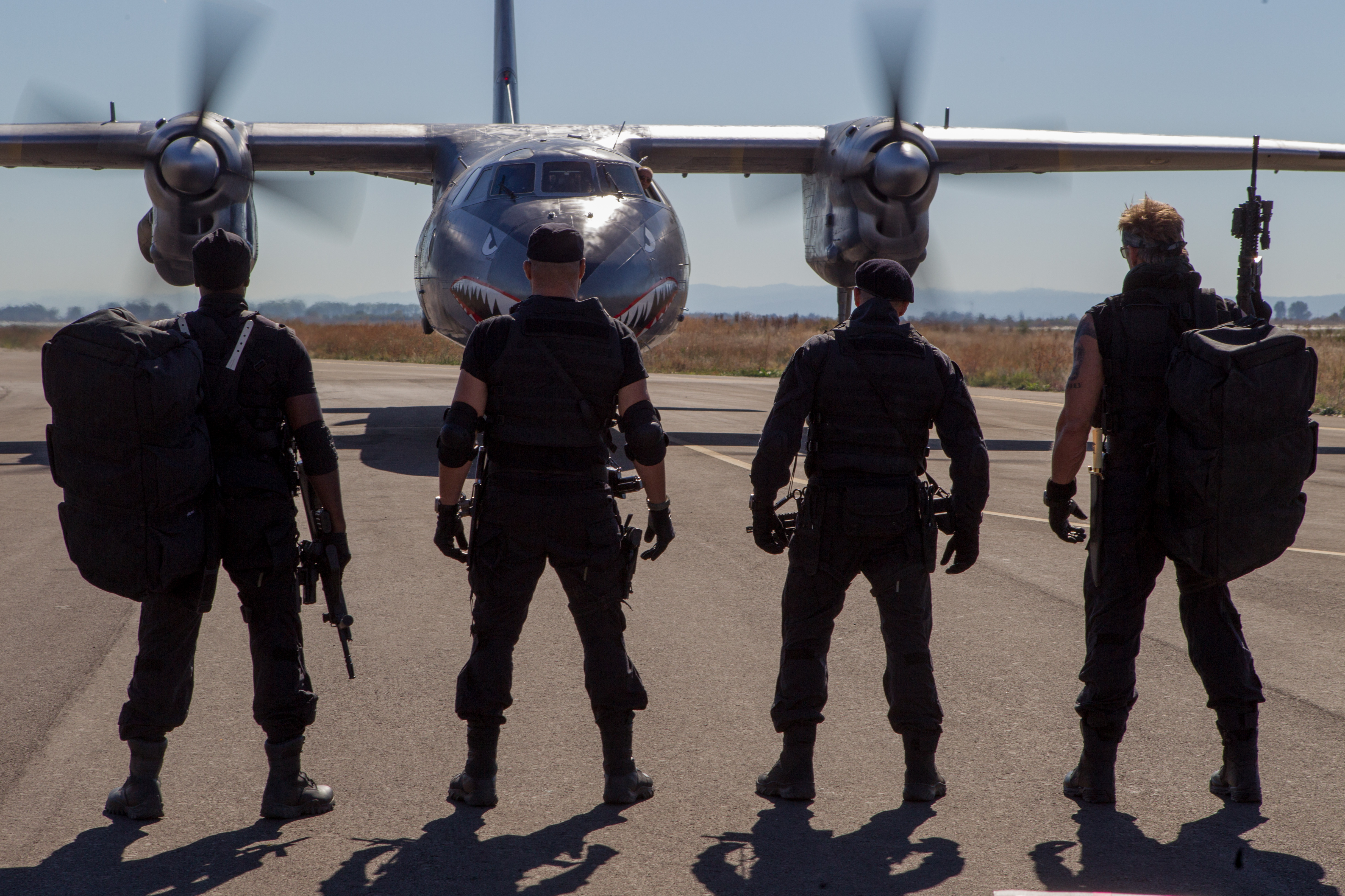 Four soldiers with rifles and backpacks in front of a plane HD Wallpaper