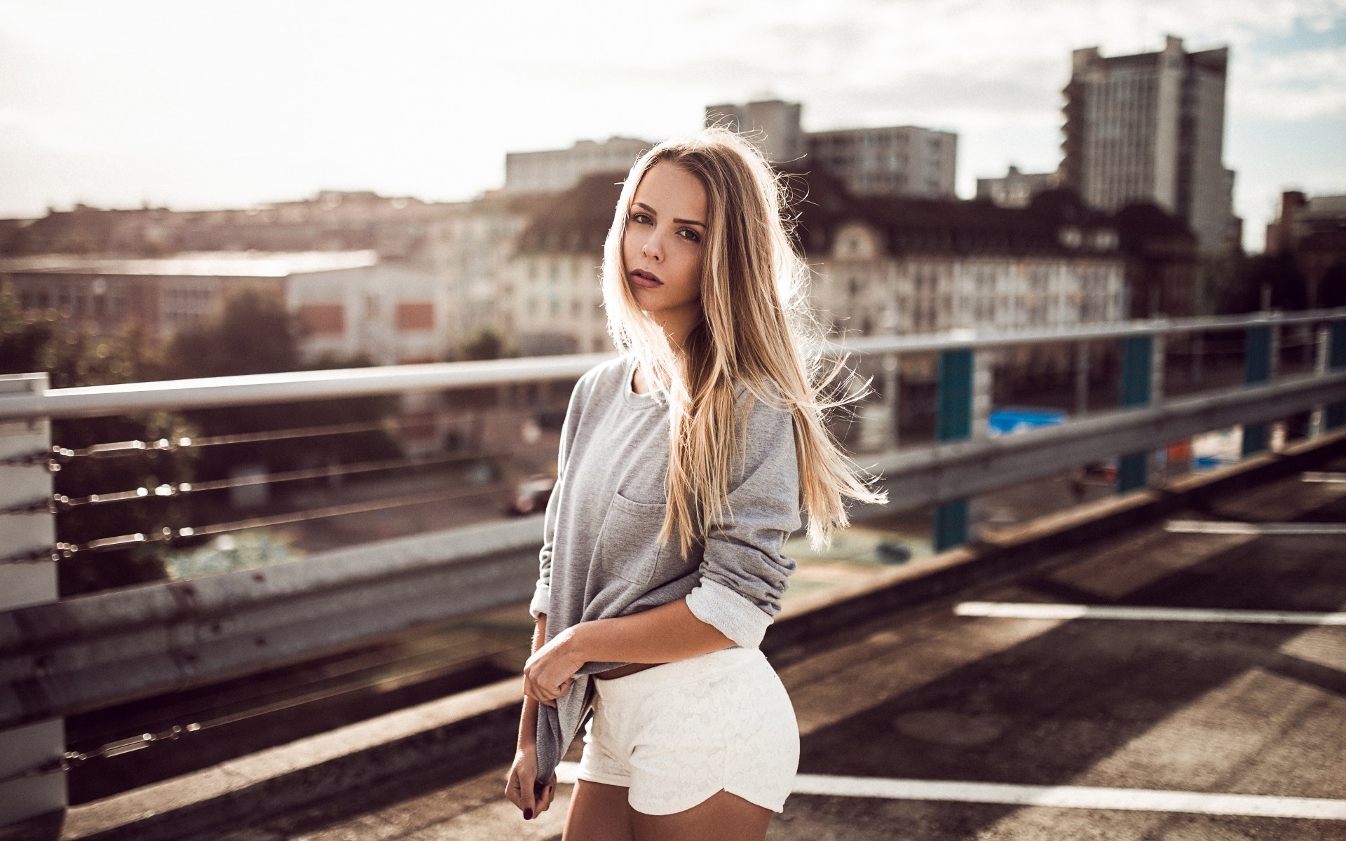 Woman in grey sweatshirt and white shorts on a rooftop HD Wallpaper