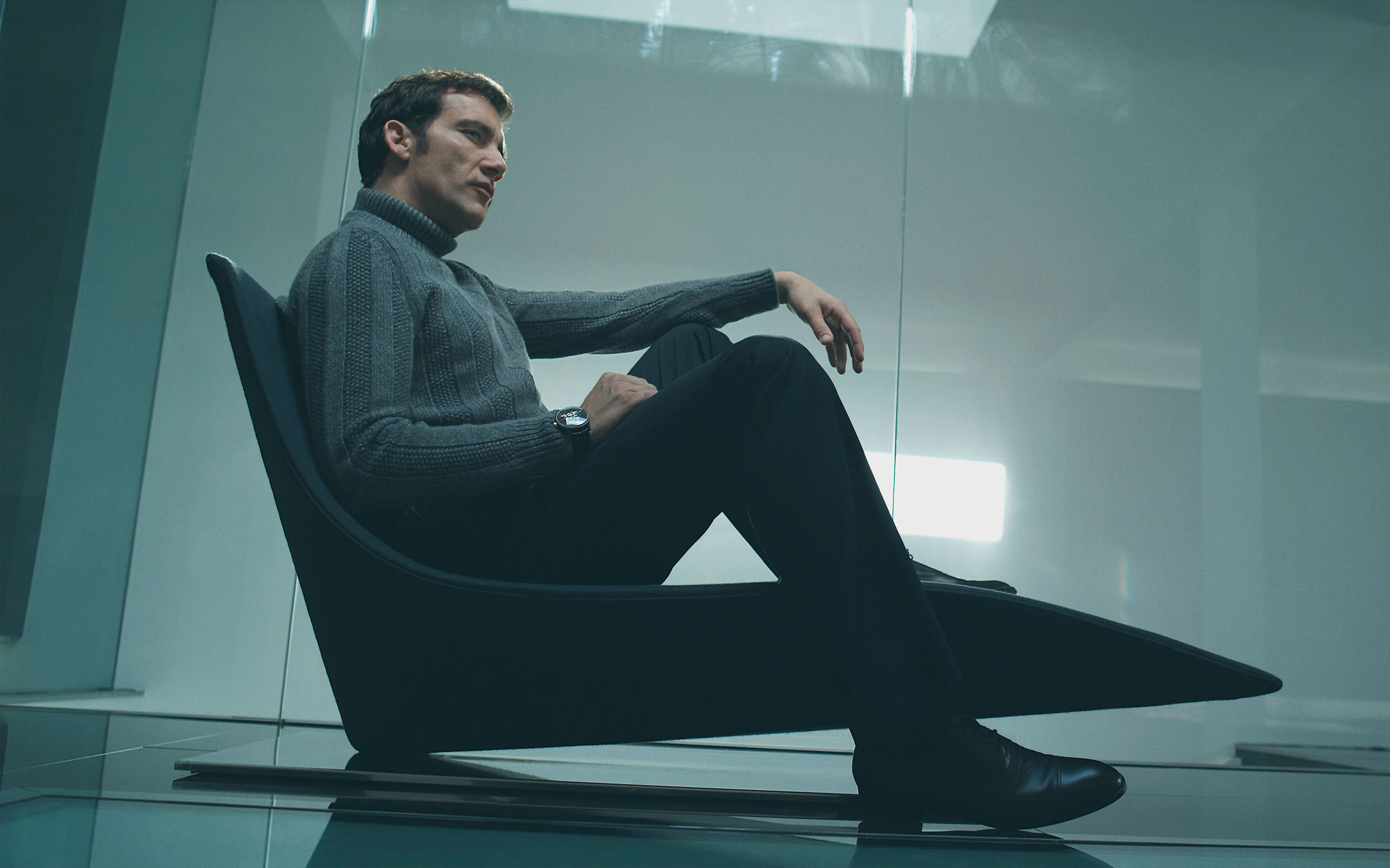 Clive Owen sitting in a modern chair HD Wallpaper