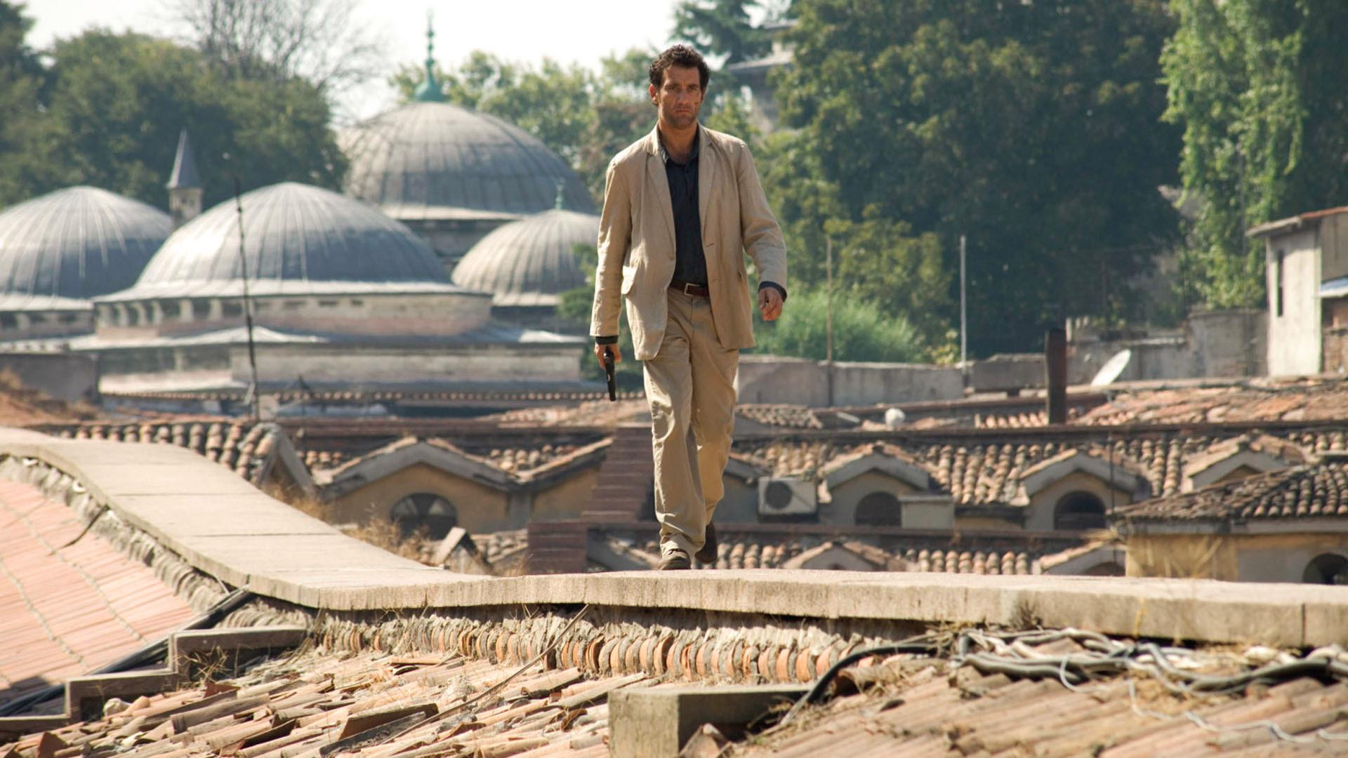 Clive Owen walking on a rooftop with a gun HD Wallpaper