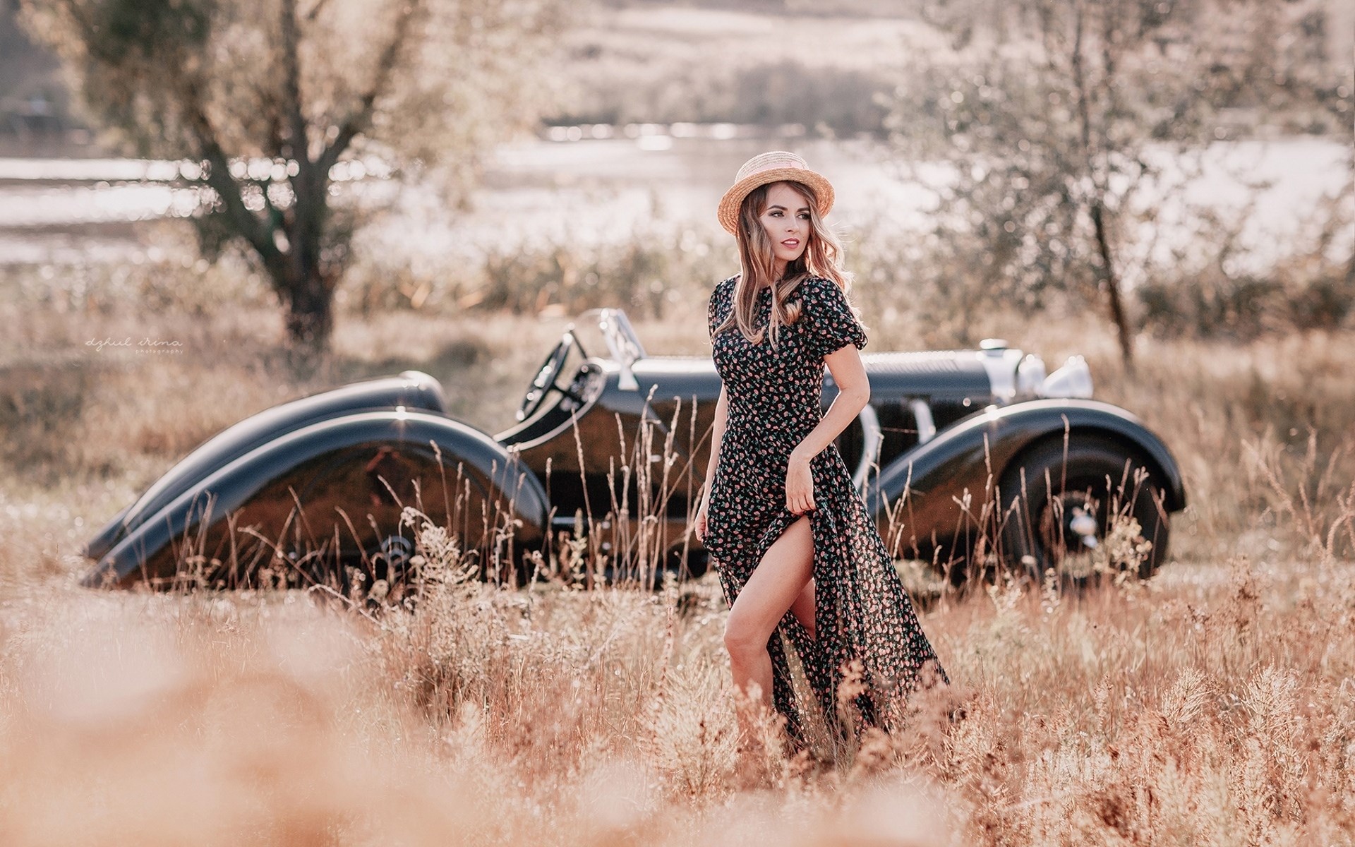 Woman in floral dress and straw hat posing by vintage car HD Wallpaper