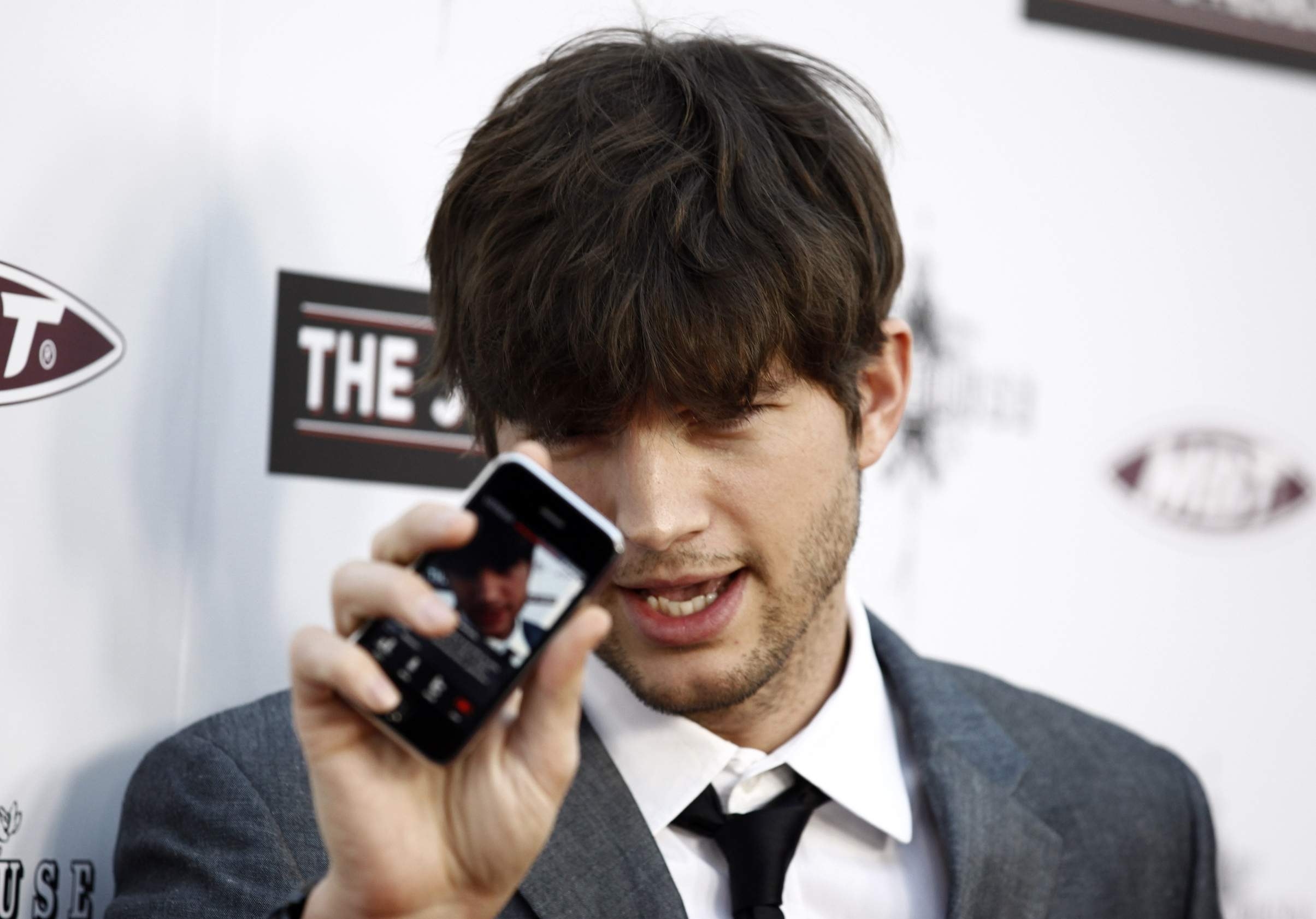 Ashton Kutcher holding a smartphone HD Wallpaper