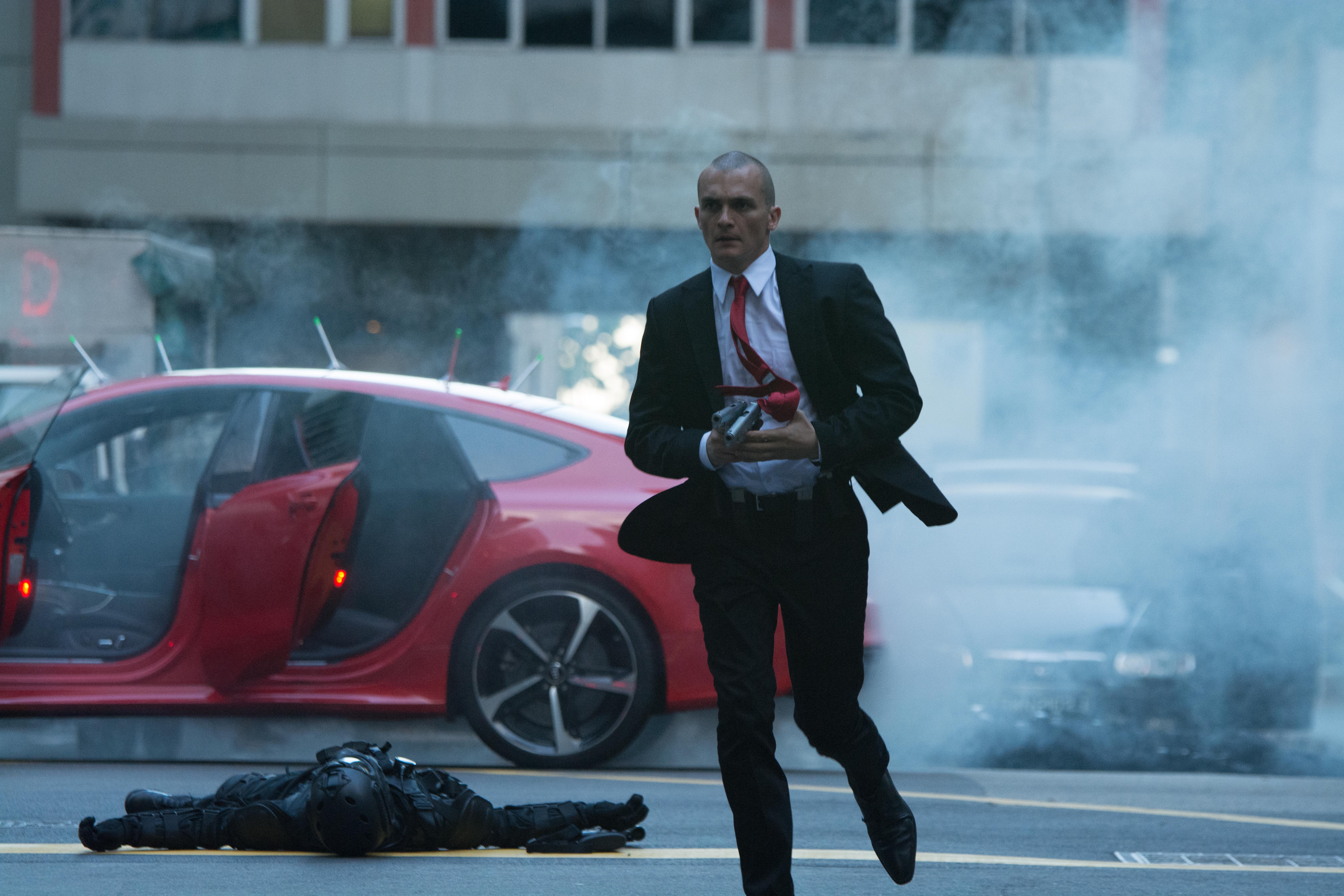 Rupert Friend in a suit running with a gun HD Wallpaper