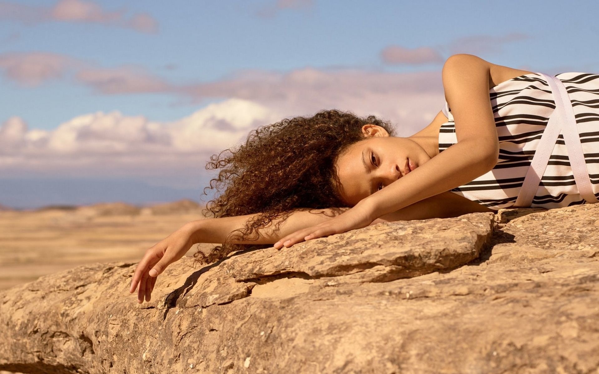 Young woman lying on rocks in a desert landscape HD Wallpaper