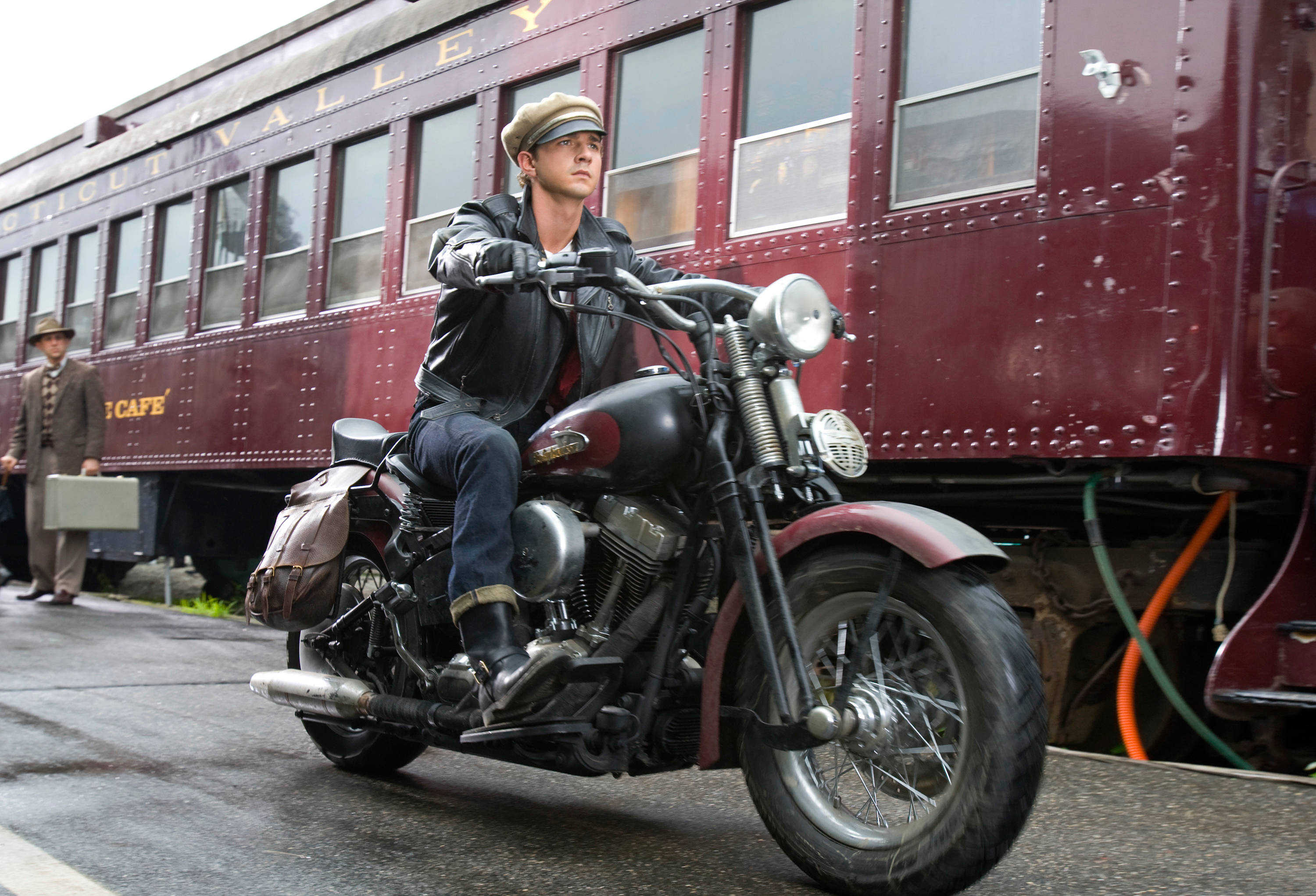 Shia LaBeouf riding a motorcycle near a train HD Wallpaper