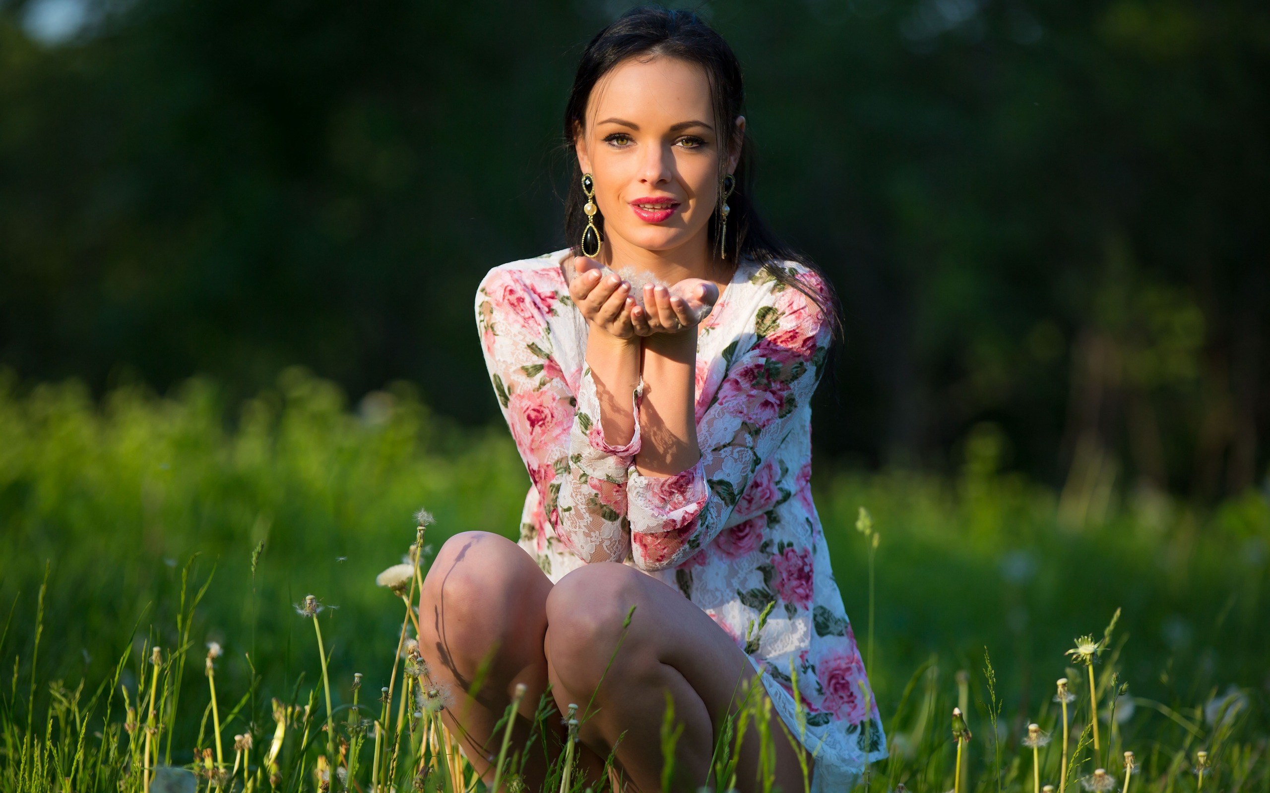 Woman in floral dress blowing dandelion seeds in a field HD Wallpaper