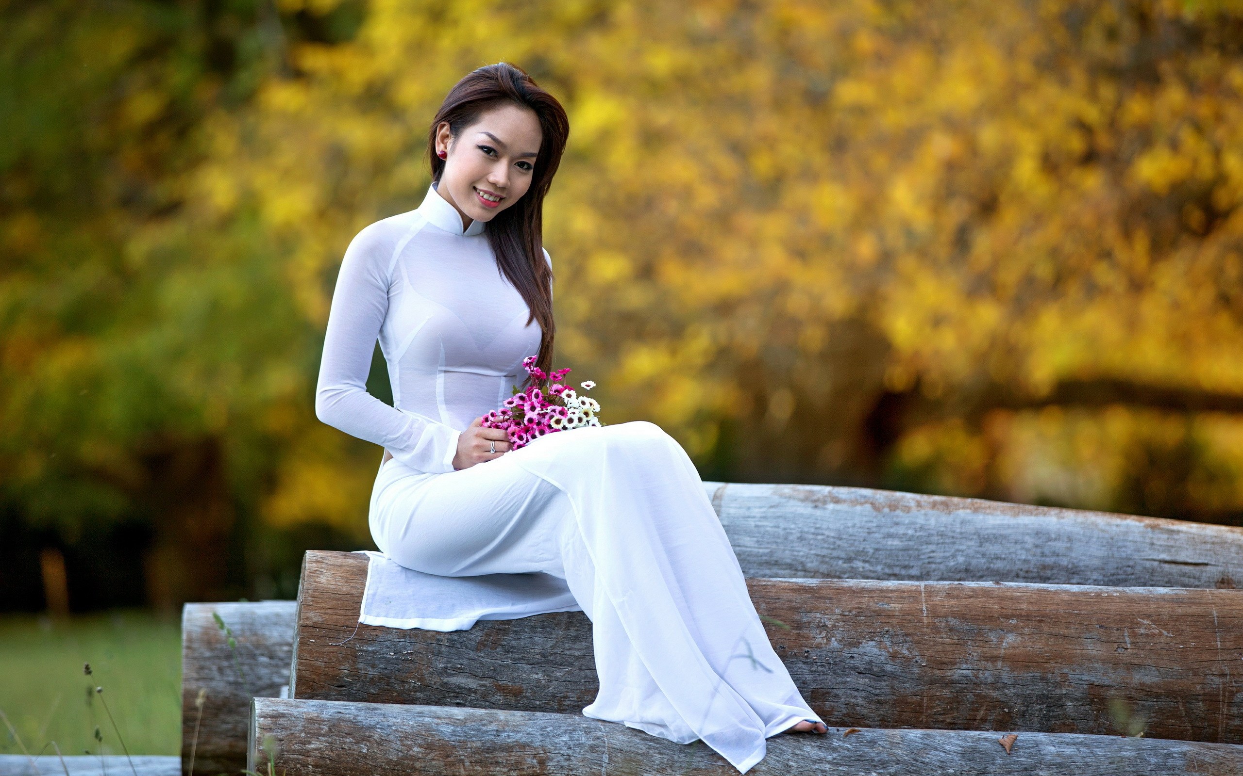 Woman in white dress holding flowers sitting on logs HD Wallpaper